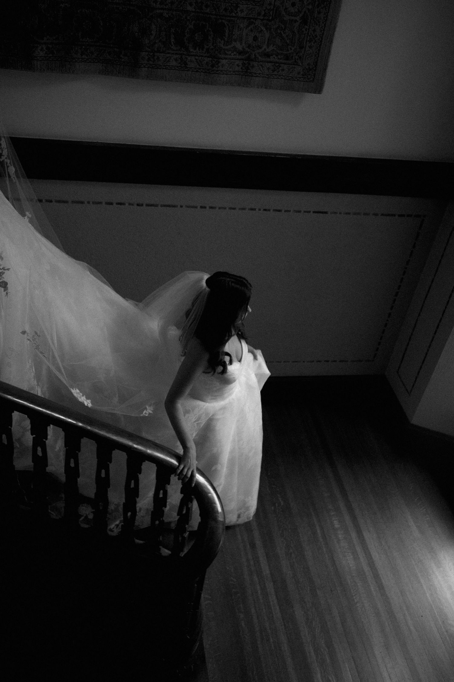 Bride in flowing white gown and veil descends grand staircase in dramatic lighting.
