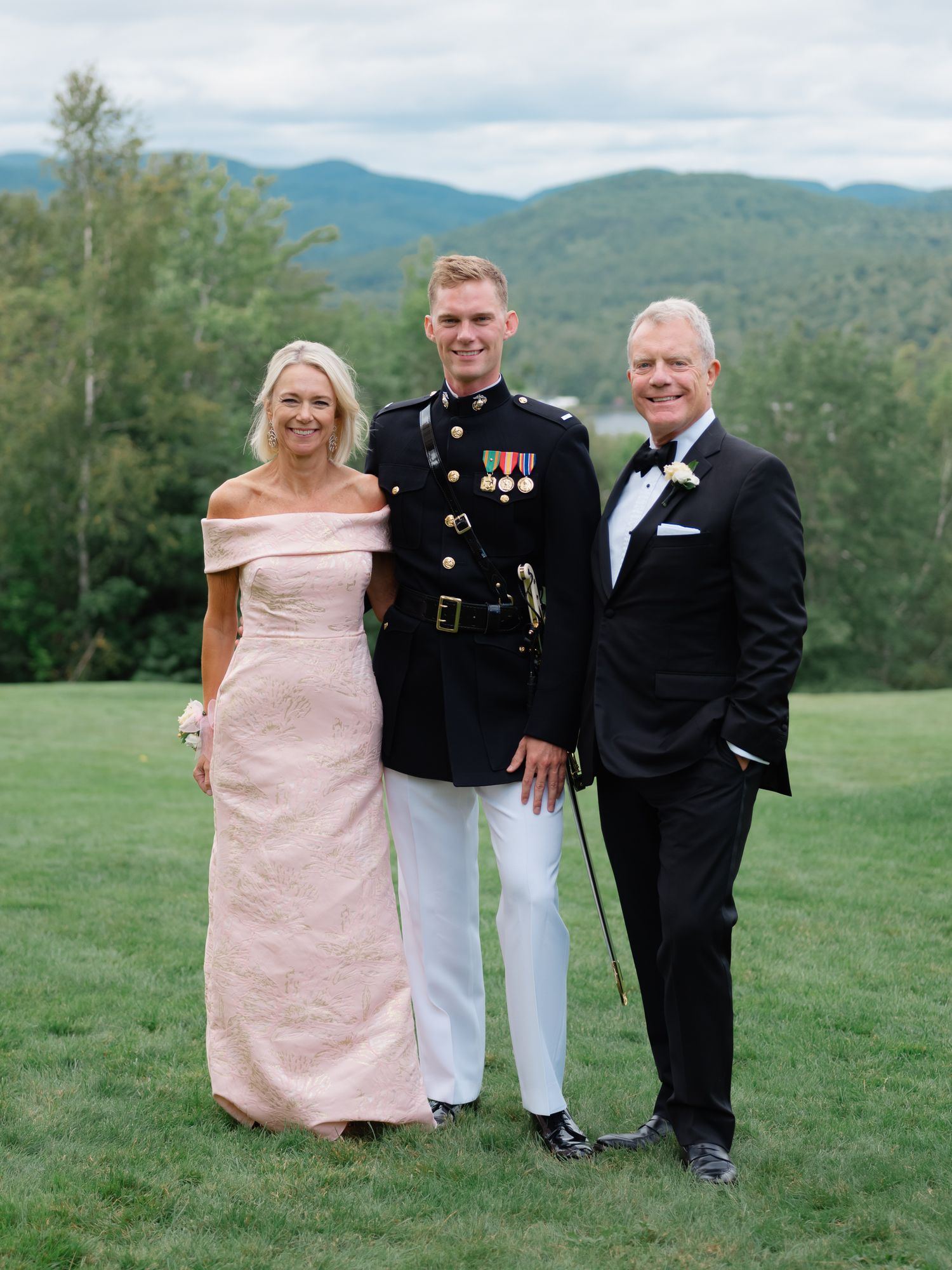 Marine groom posing with parents against mountain backdrop.