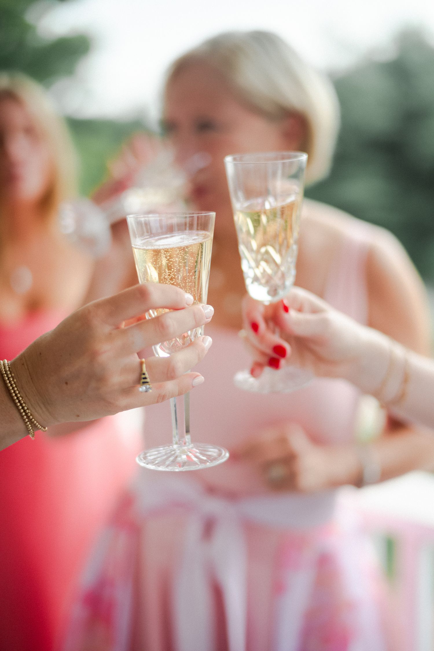 Women in pink dresses toasting with crystal champagne glasses at an outdoor wedding celebration.