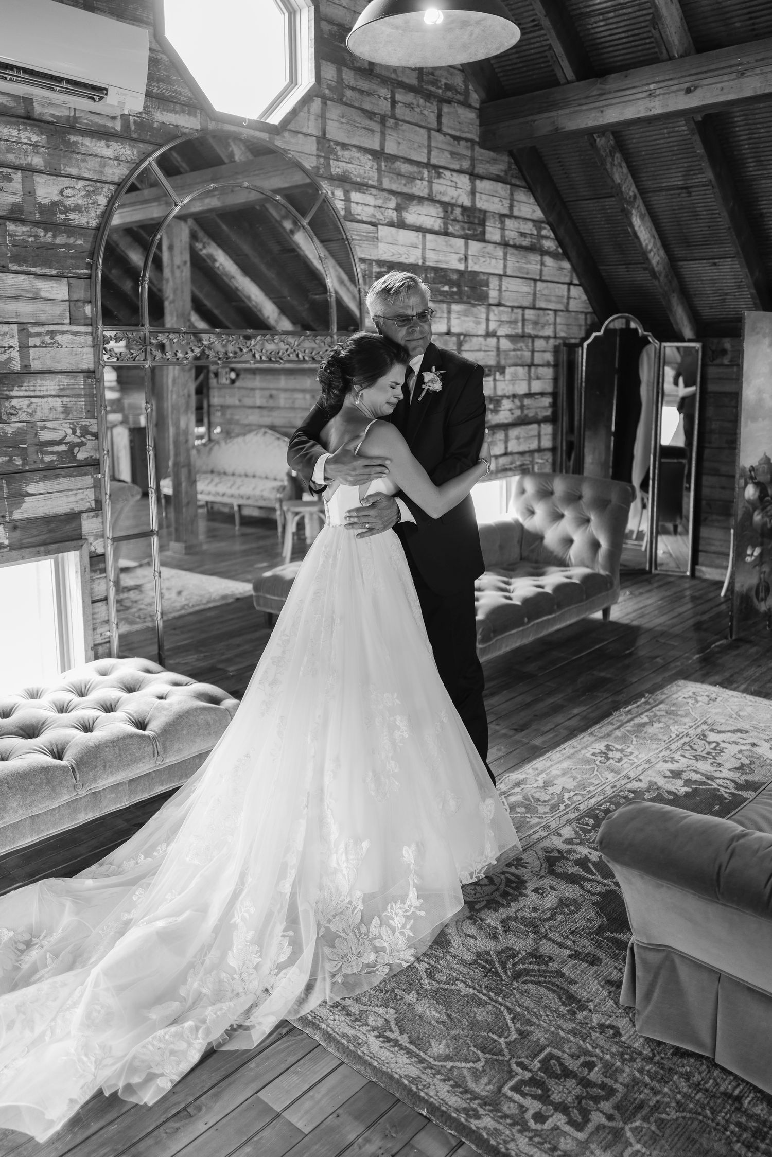 Bride in lace ball gown sharing tender embrace with father in rustic stone venue interior.