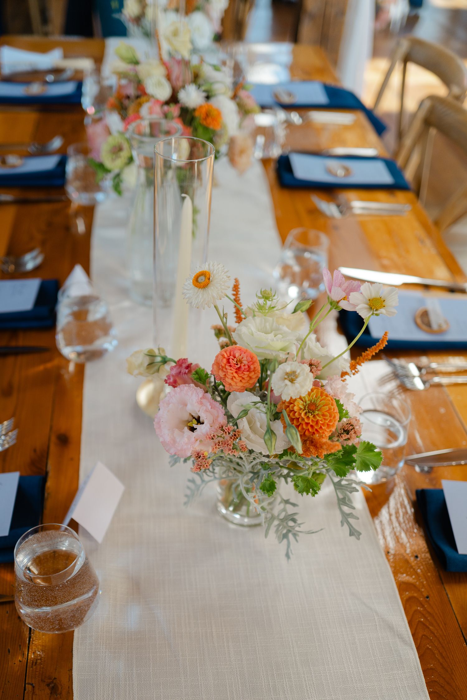 Elegant farm table centerpiece with pink, orange, and white flowers on a white linen runner.