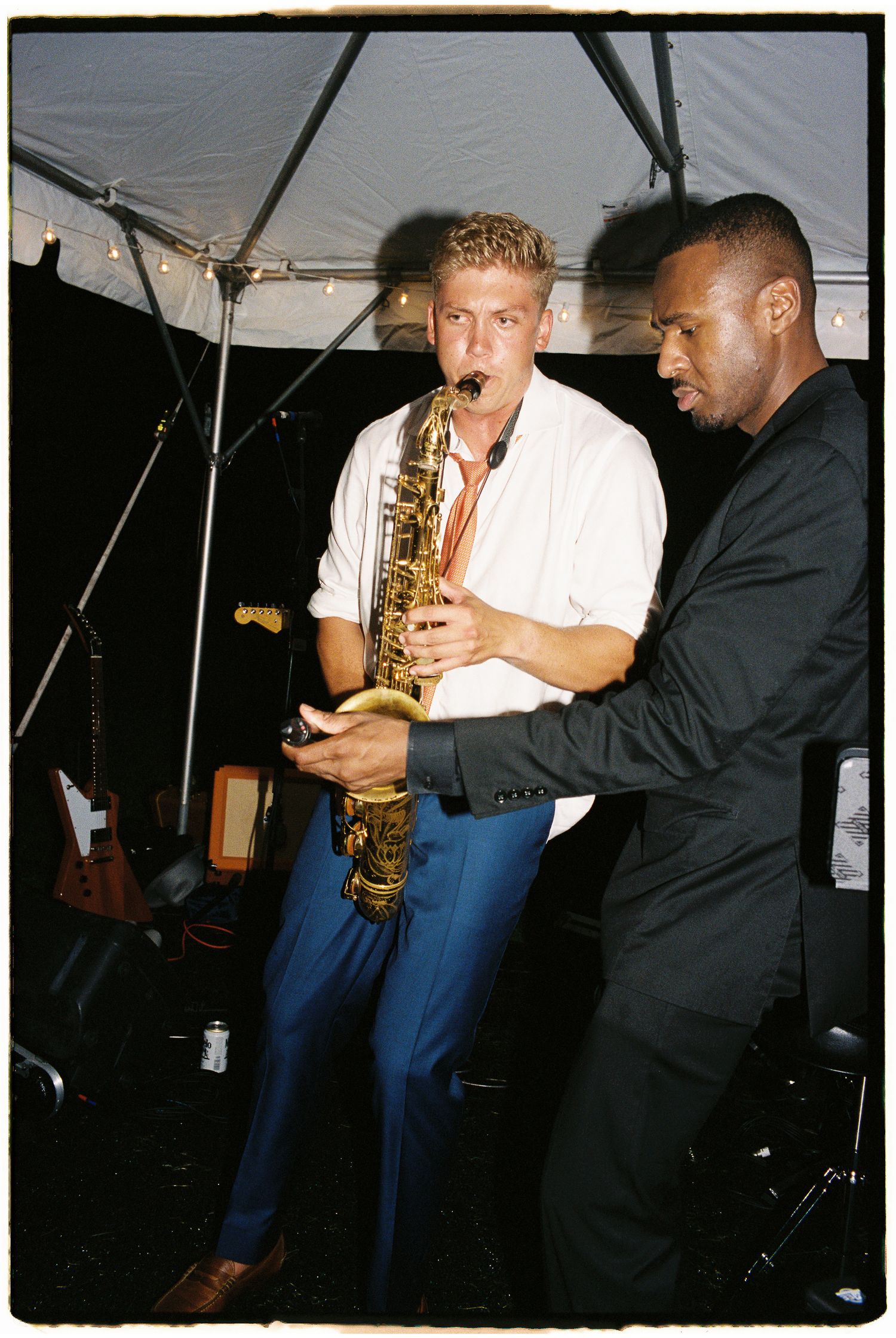 Two musicians perform with a saxophone under a tent at a live wedding band performance.