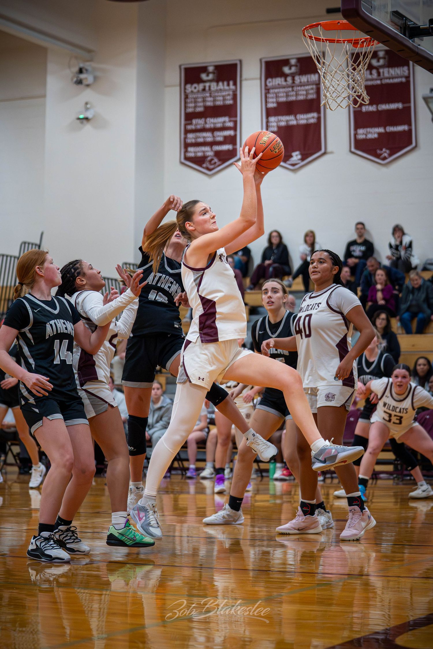 Female basketball player leaps for a layup during a high school girls game in a maroon gymnasium.
