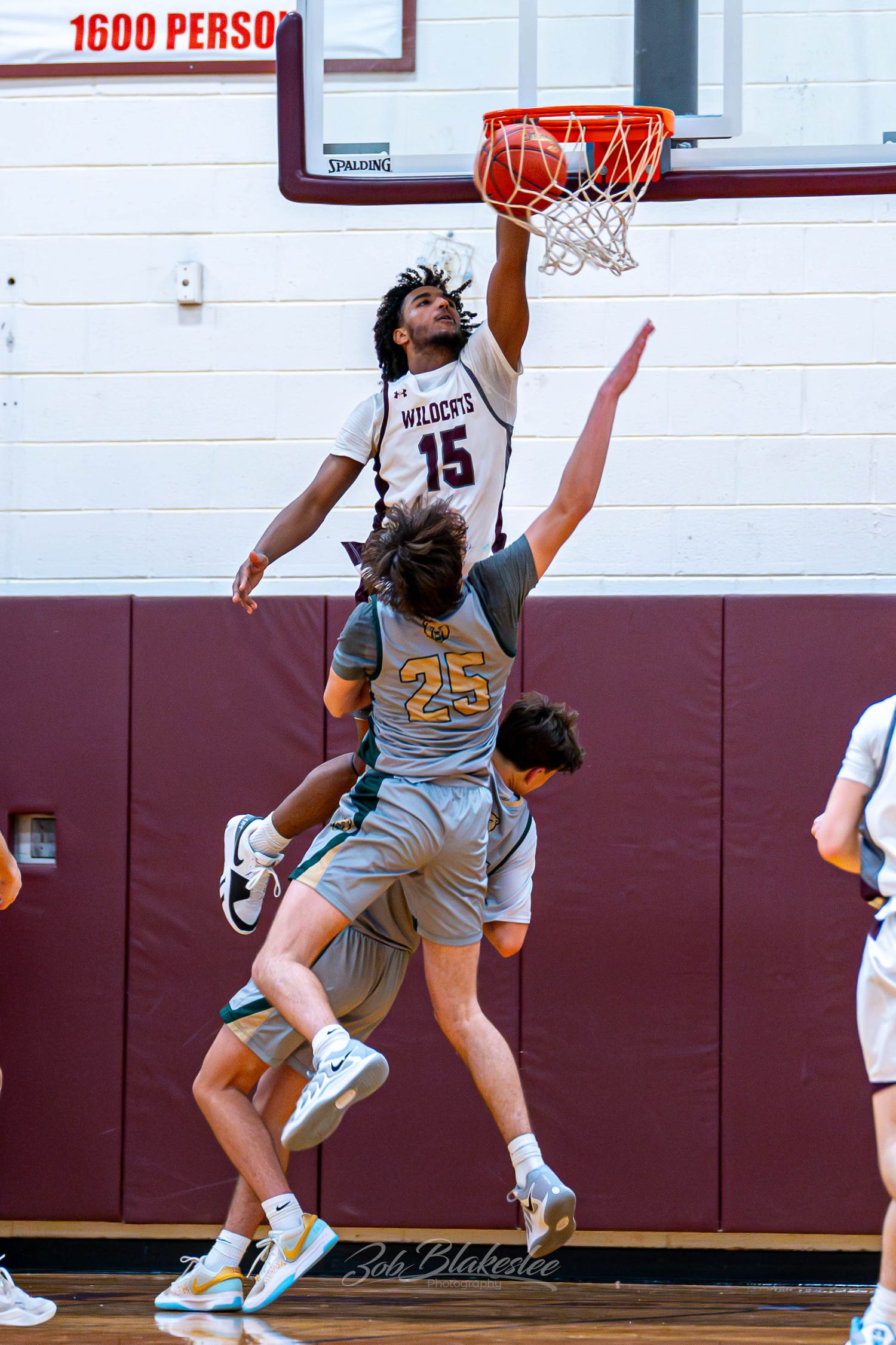 A Wildcats basketball player #15 dunks over a defender during an indoor high school game.