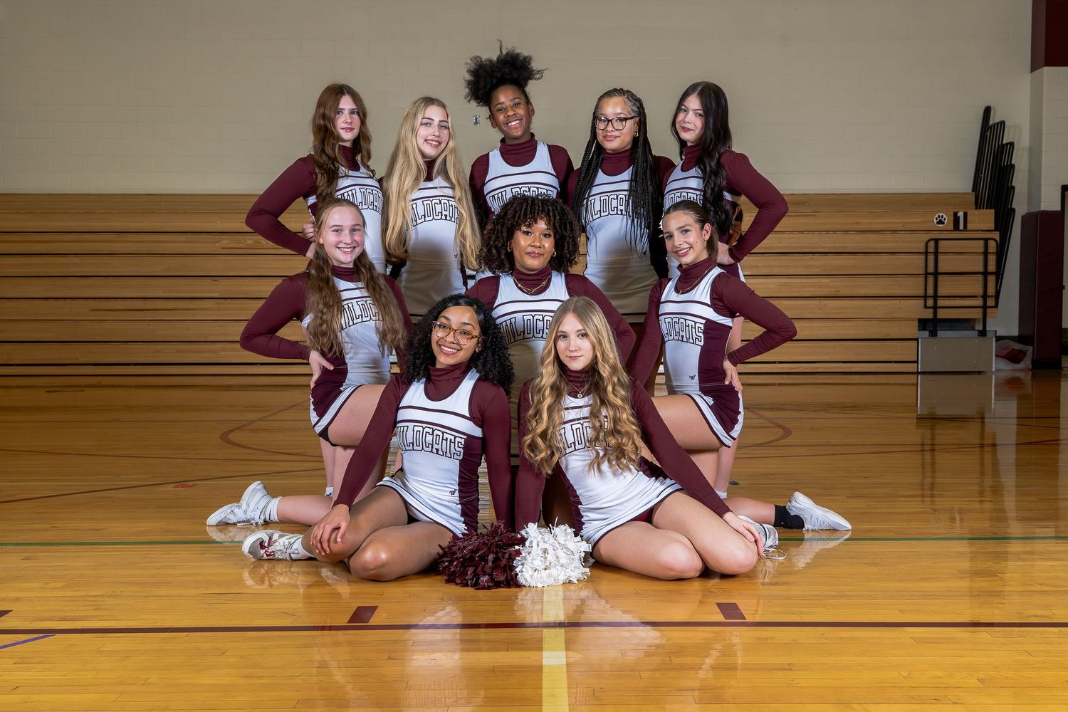 High school cheerleading squad poses for team photo in maroon and white uniforms on gymnasium floor.