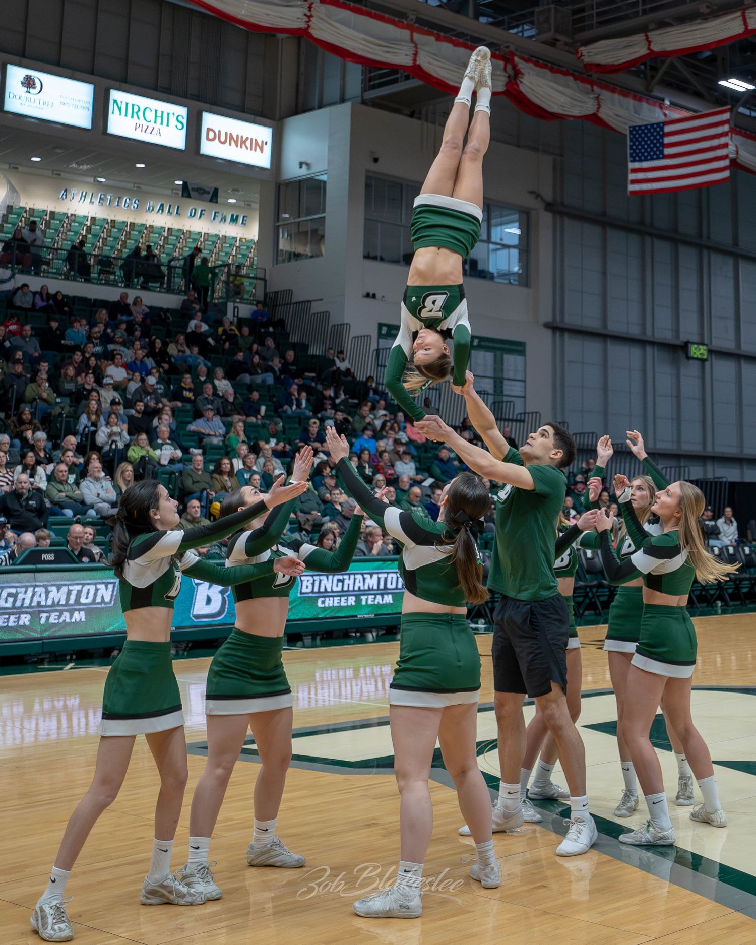 Binghamton cheerleaders perform a stunning stunt tossing a flyer into the air during a game.