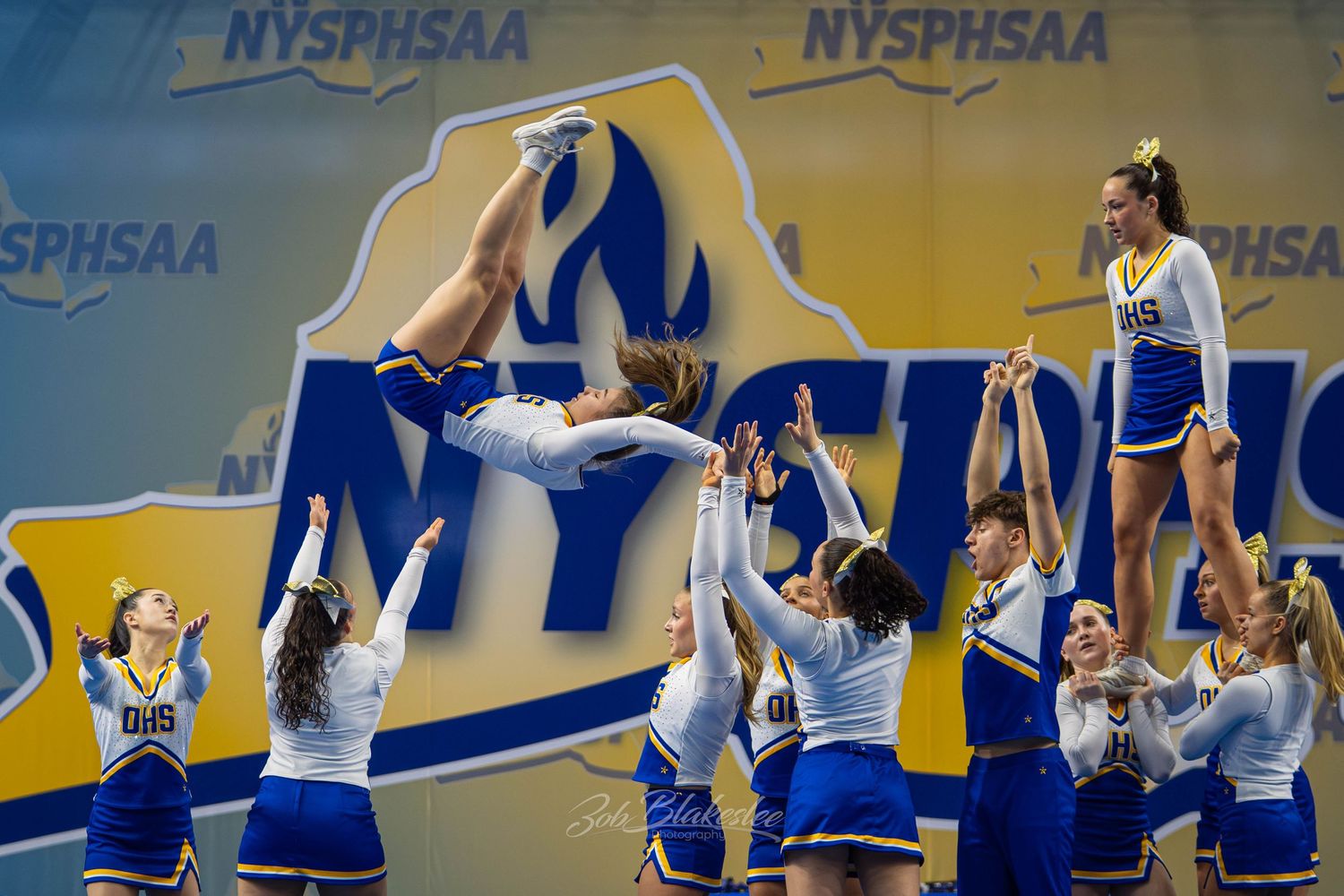 Blue and gold cheerleading squad executing impressive multi-level stunts at NYSPHSAA Championships.
