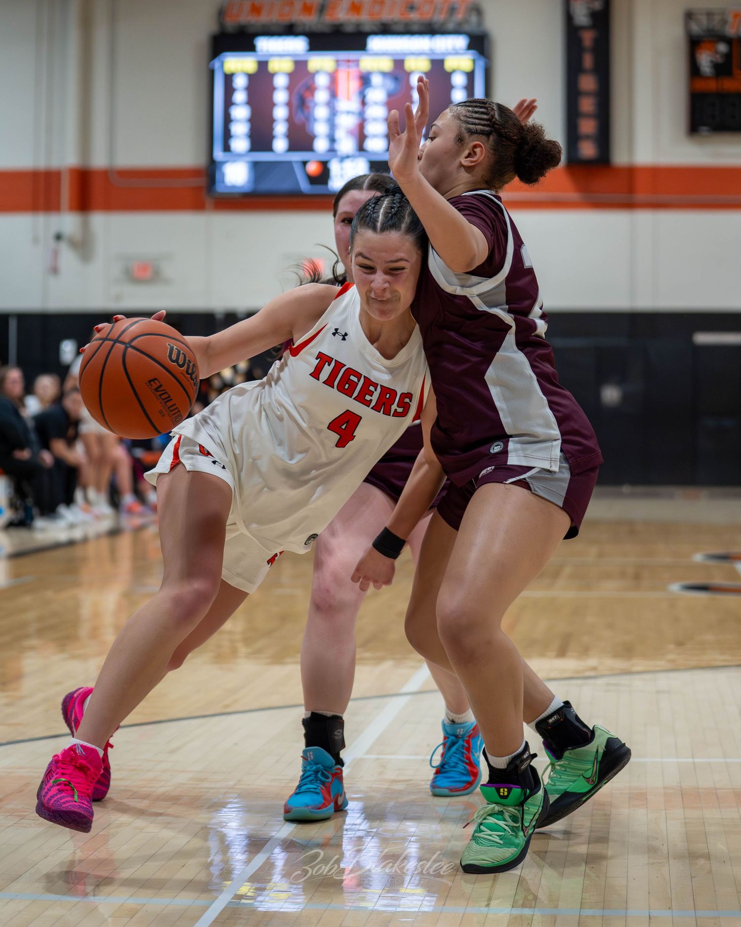 Tigers #4 drives to the basket against a defender in a girls high school basketball game on a home court.