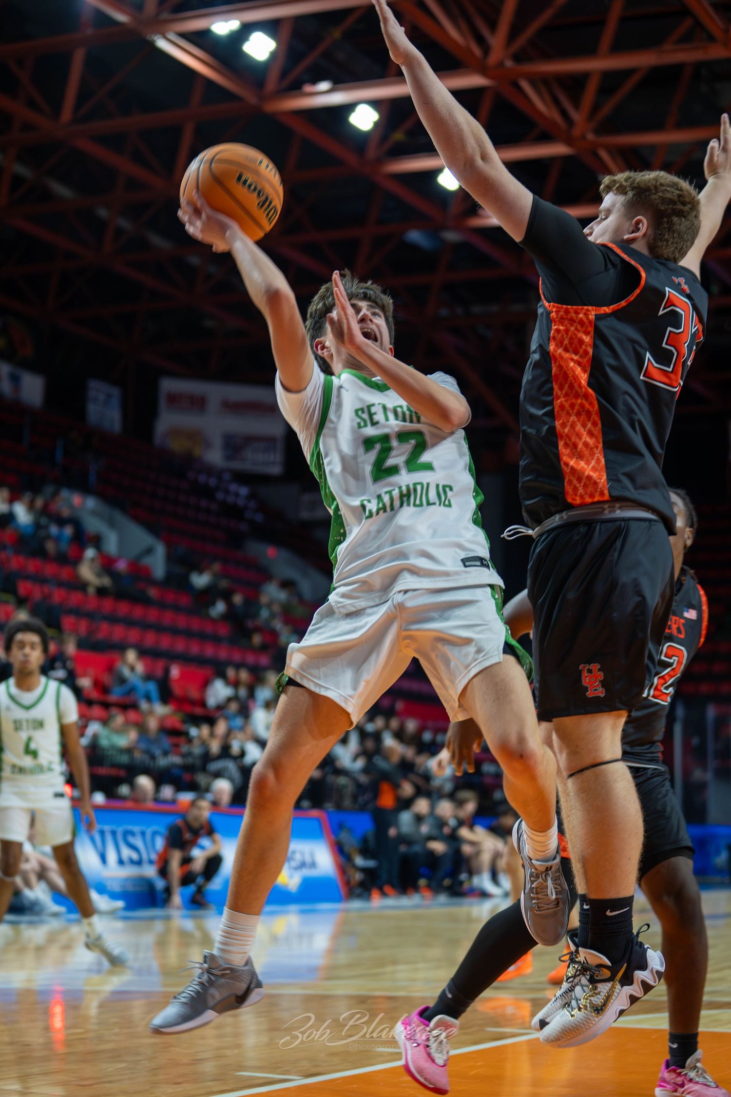 Seton Catholic #22 attempts a layup against a defender in an orange uniform during a high school basketball game.