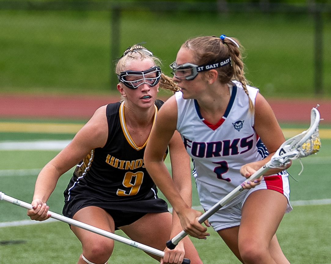 Two female lacrosse players compete for possession during an intense outdoor lacrosse game.
