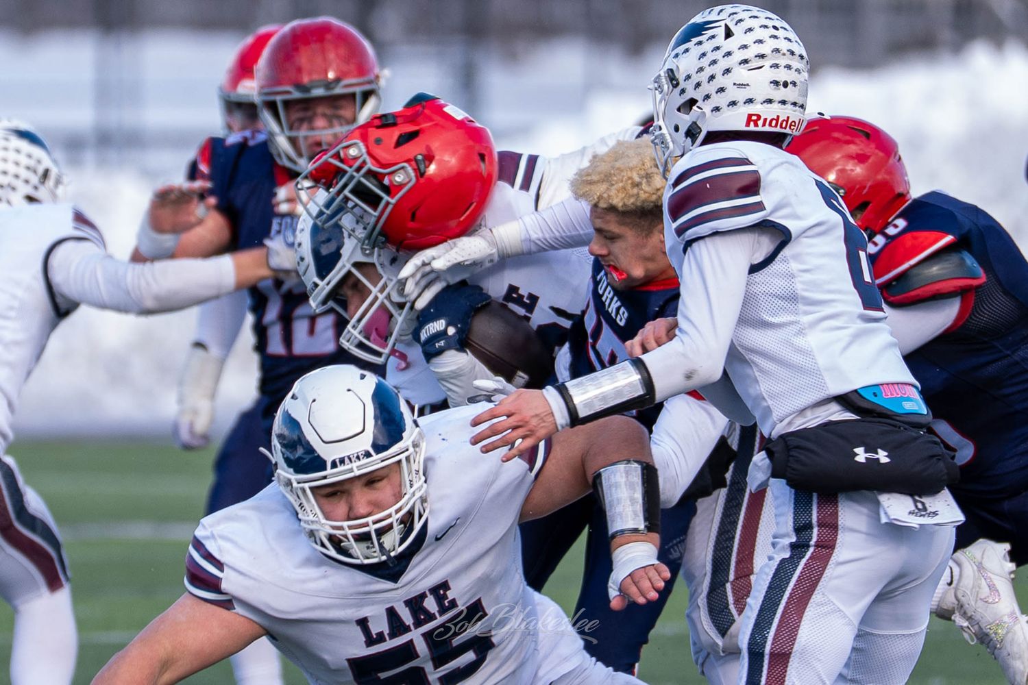 Football players from opposing teams collide in a fierce tackle during a cold weather high school game.