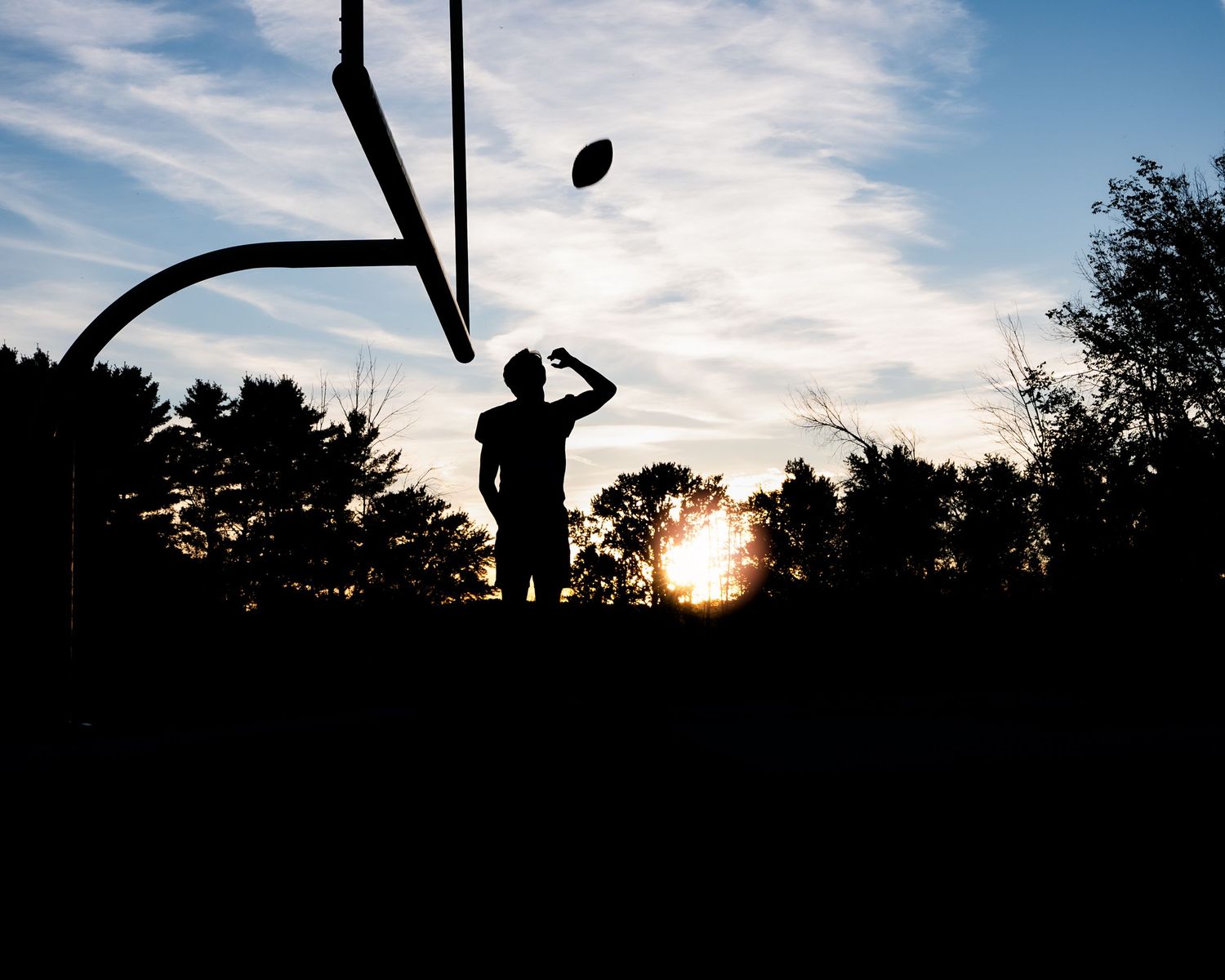 Silhouette of a football player throwing near a goalpost at sunset with trees in background.