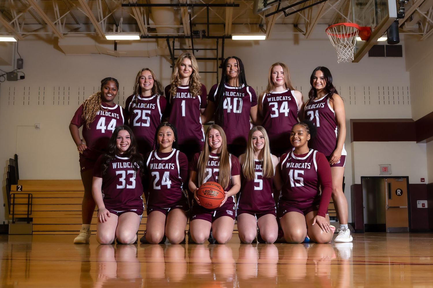 Girls high school basketball team poses for official team photo in maroon uniforms on indoor court.