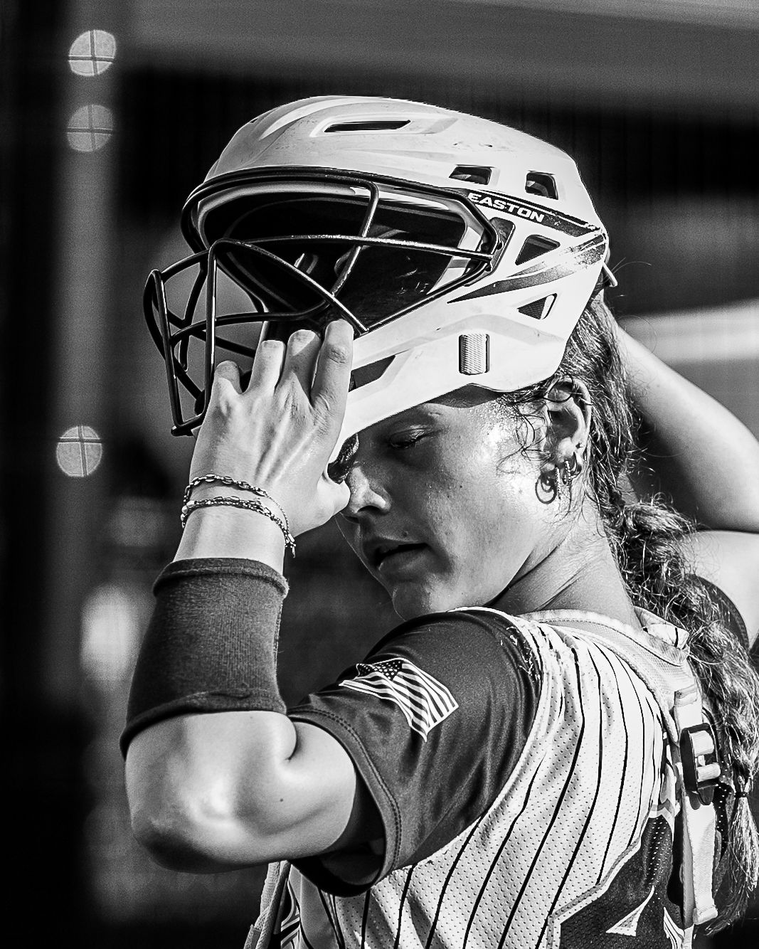 Female softball catcher adjusts white Easton helmet in black and white close-up portrait photo.
