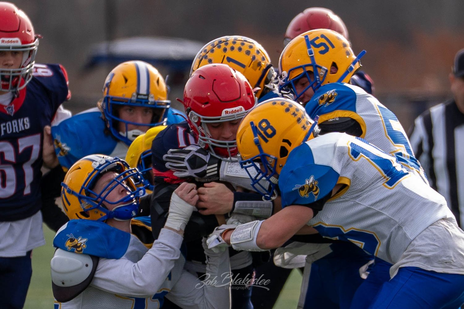 High school football player in red helmet is tackled by multiple defenders in yellow jerseys.