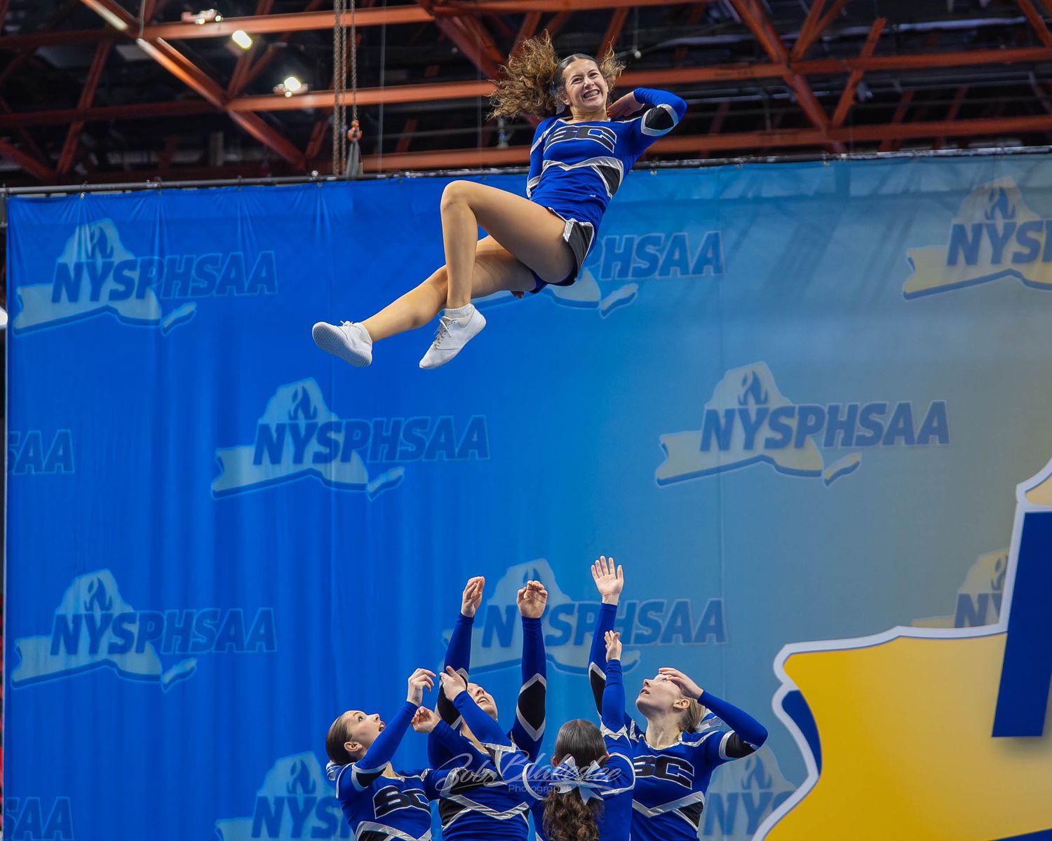 Blue uniformed cheerleader launched high into air during NYSPHSAA championship competition.