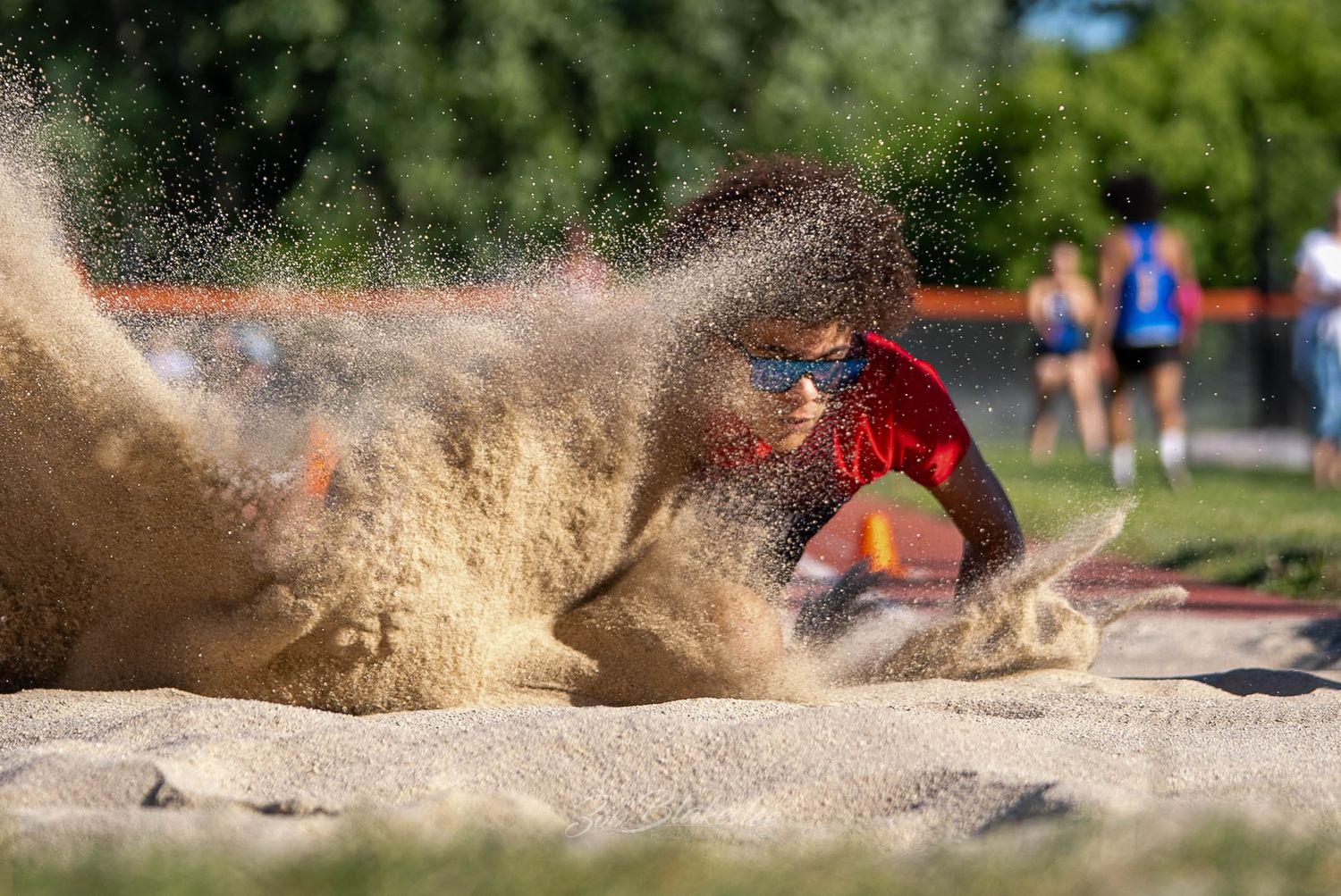 An athlete lands in a sand pit creating a dramatic splash during a long jump competition.