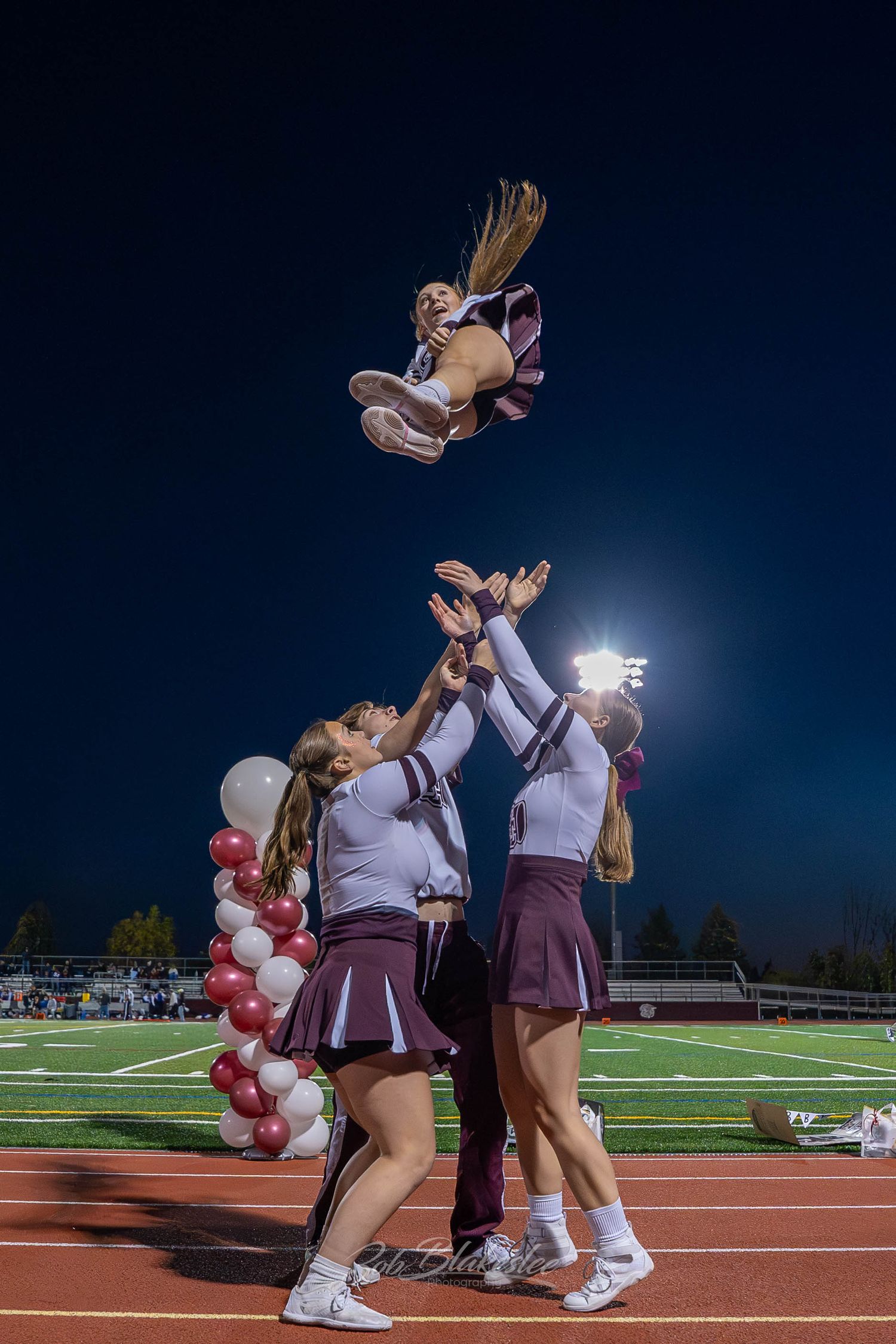 Cheerleaders perform a dramatic stunt tossing a teammate high into the night sky at a football game.