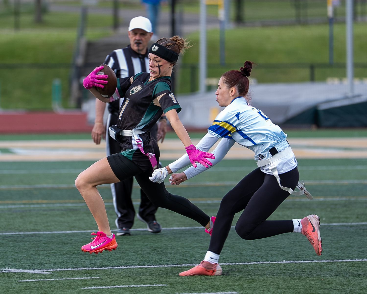 Women playing flag football on a green turf field, with a referee watching the action closely.