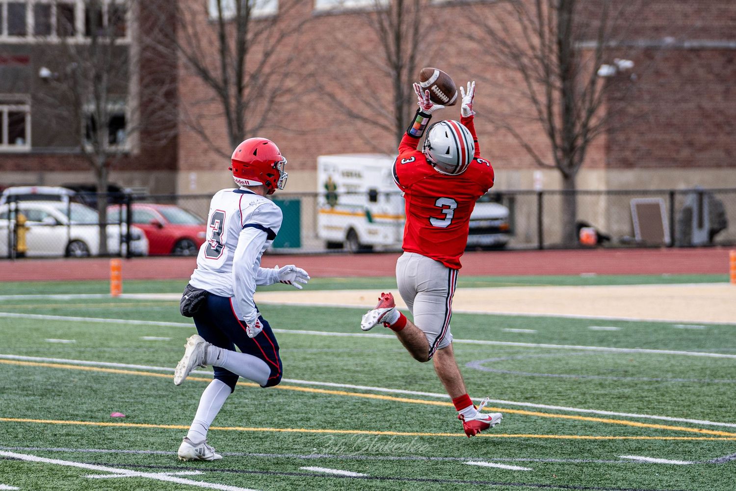High school football player in red jersey catches a pass while being defended during an outdoor game.