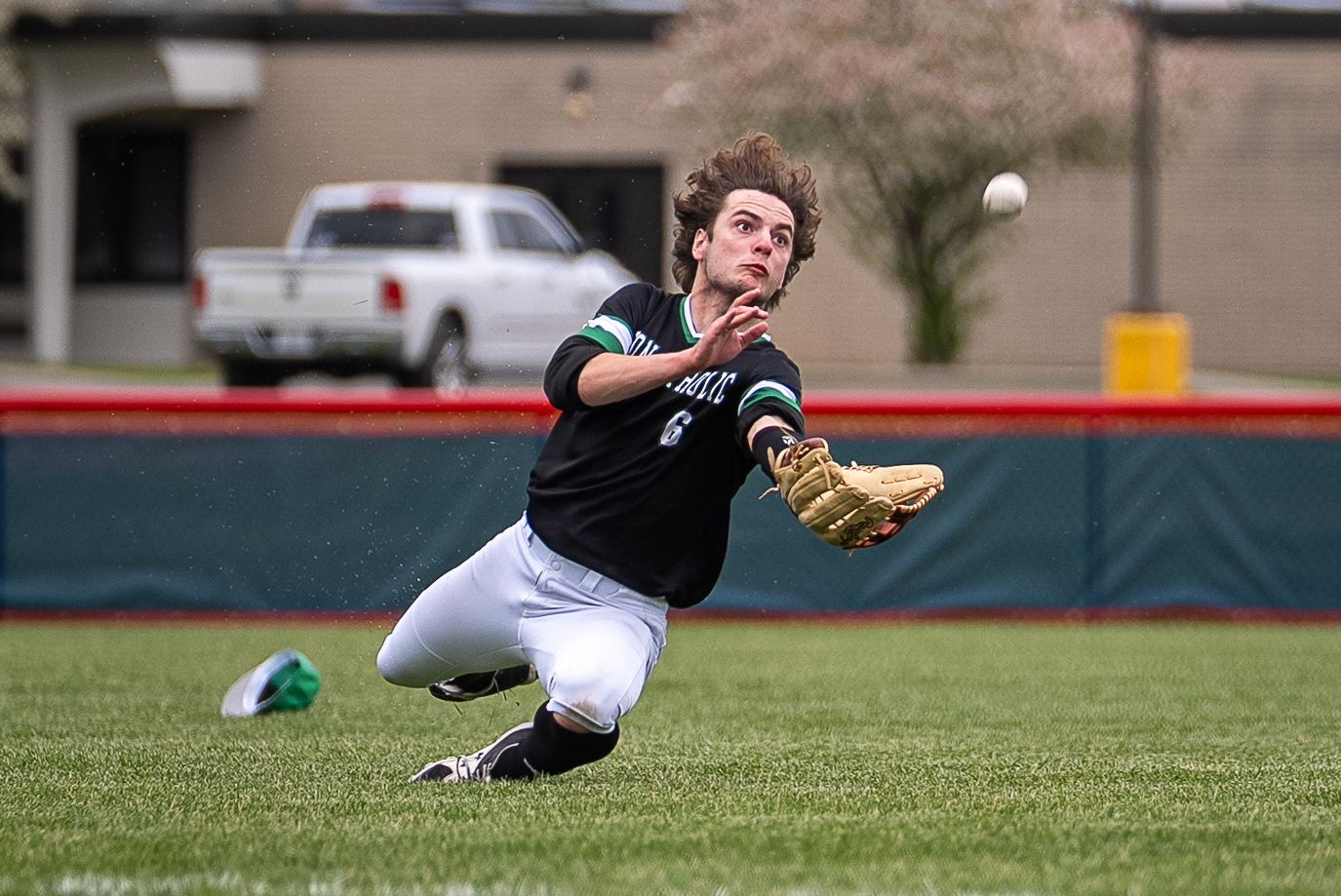Baseball outfielder makes diving catch attempt on fly ball during spring baseball game.