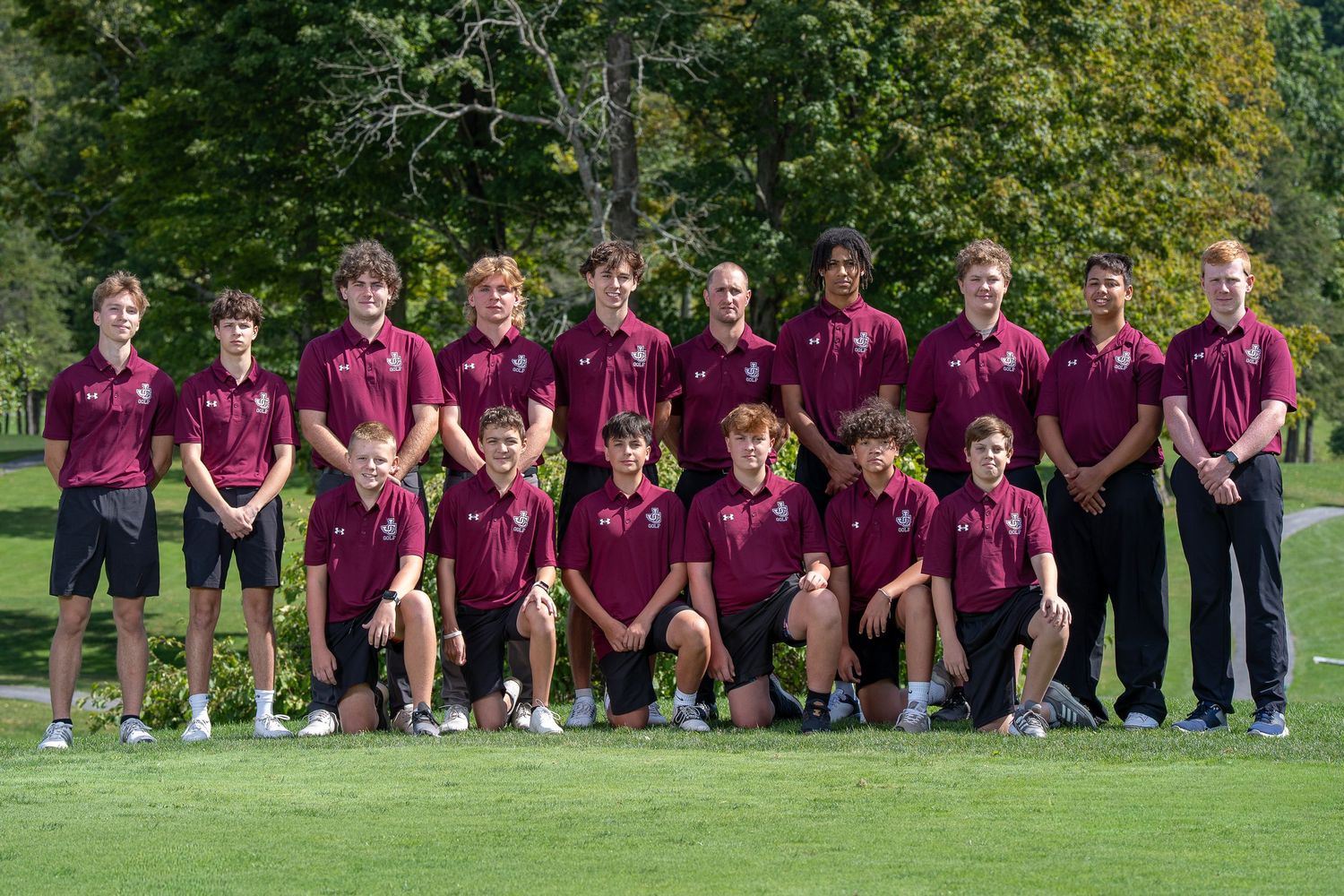 Boys golf team posing in maroon polo shirts on a green golf course for a group photo.