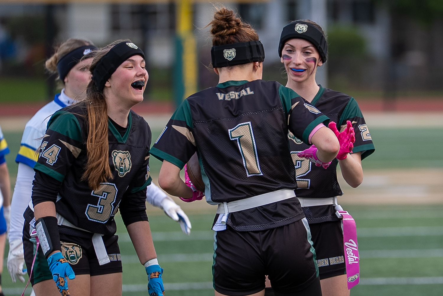 Women in black uniforms celebrate during a flag football game on a green turf field.