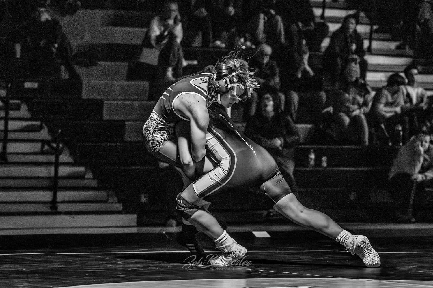 Two wrestlers compete in a dramatic black and white action photo during a high school match.