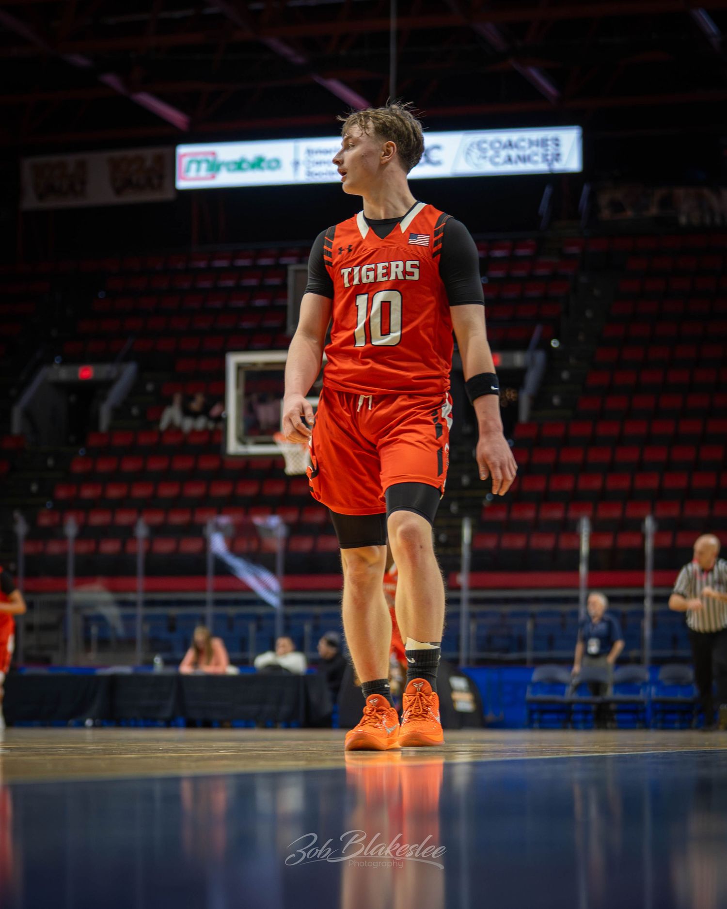 Basketball player #10 in orange Tigers jersey walks on indoor court during a game.