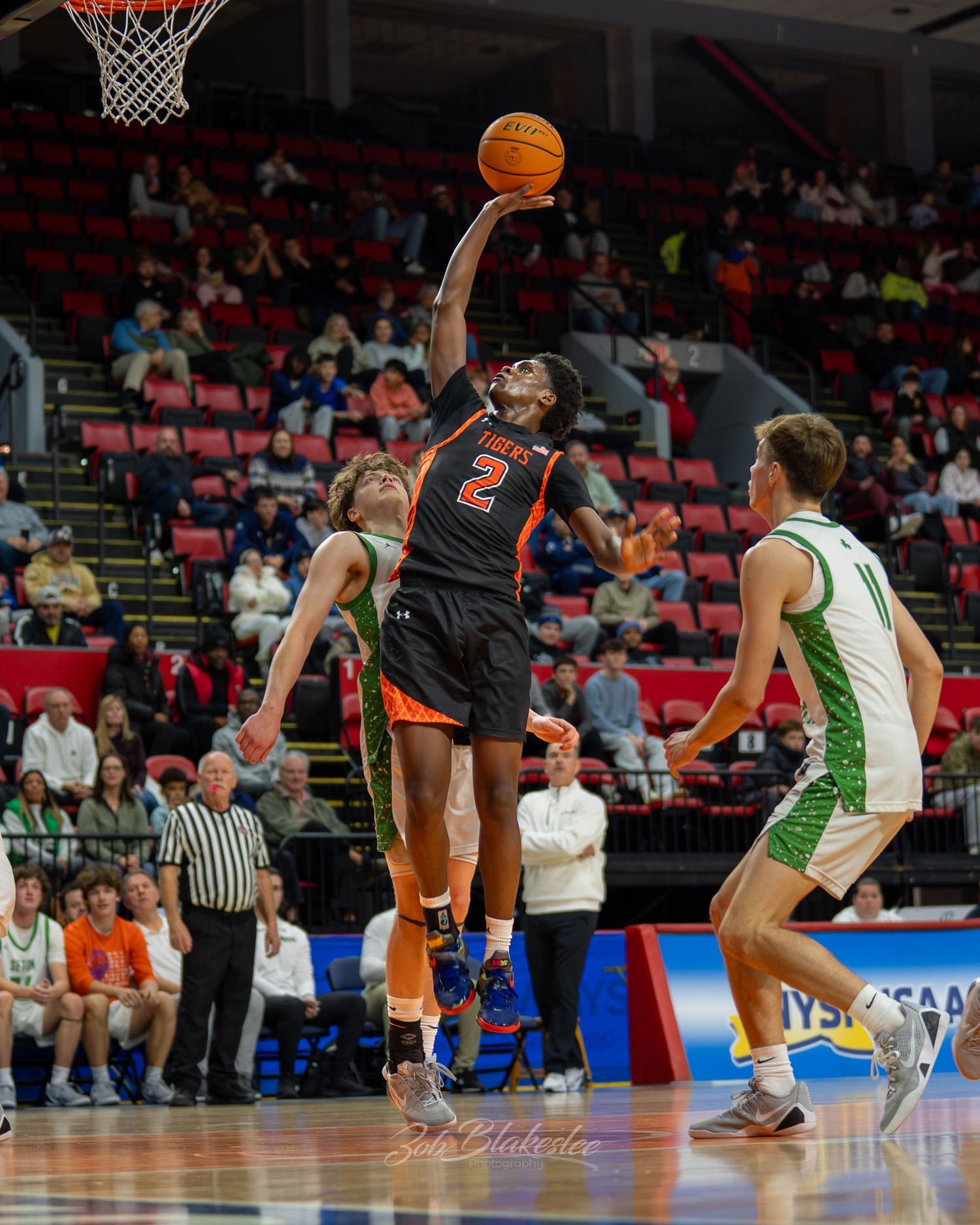 Male basketball player #2 in orange drives for a layup during a high school boys tournament game.