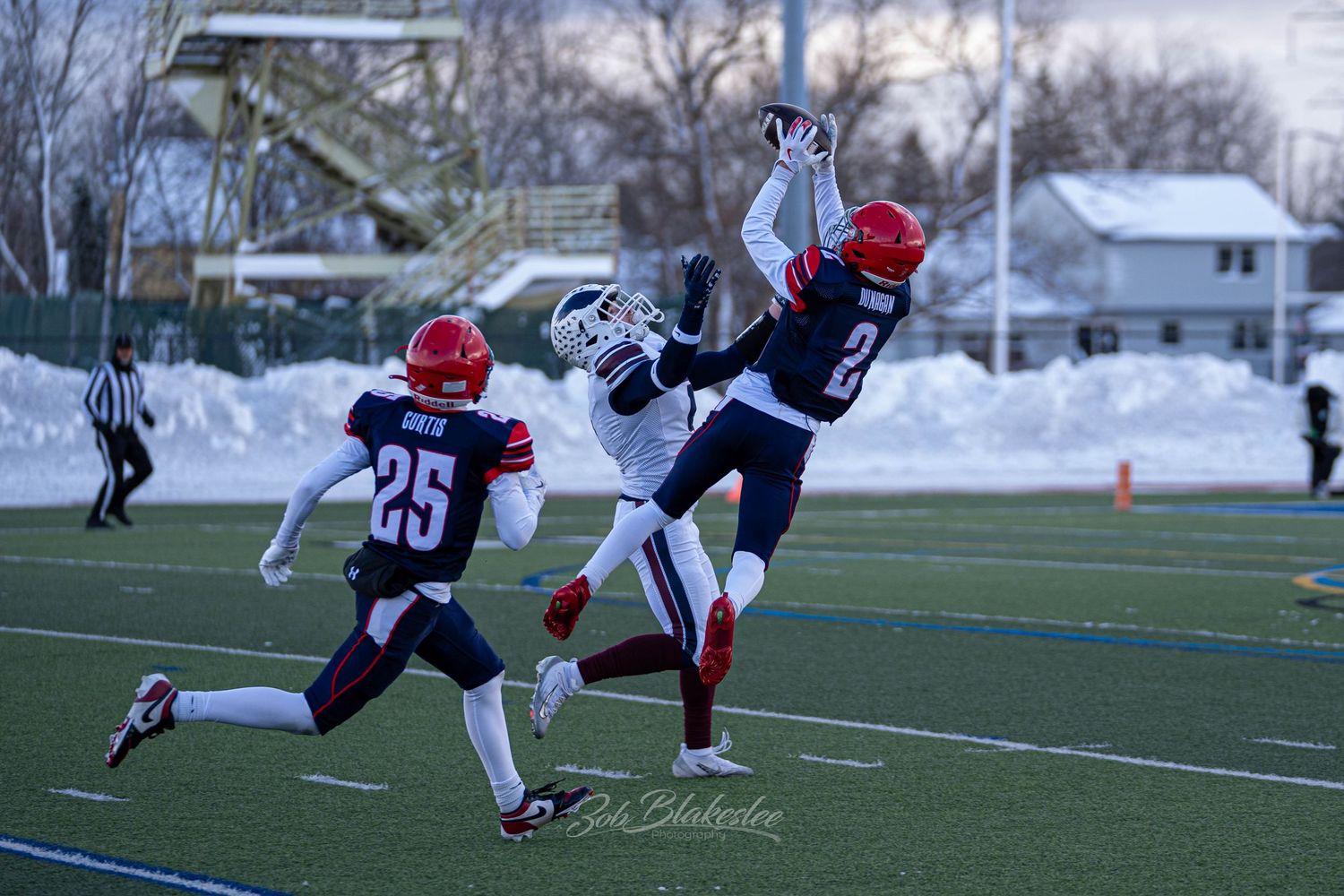 Football player leaps high to intercept a pass during a snowy winter high school playoff game.