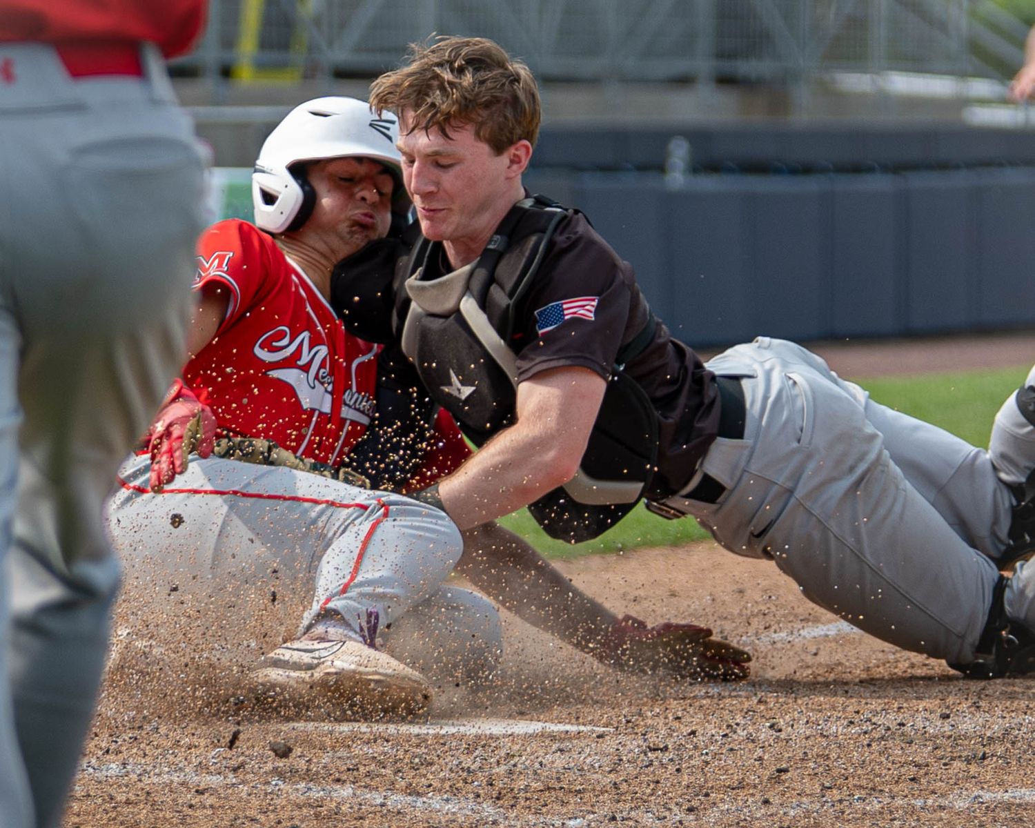 A baseball catcher tags out a sliding runner at home plate in a close play.