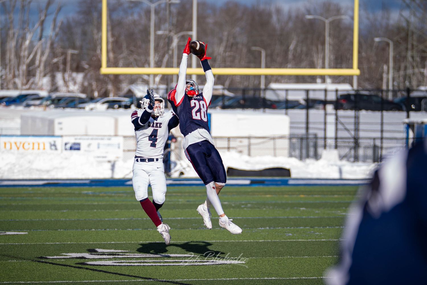 Football player in blue jersey leaps to intercept a pass against a snowy winter backdrop.