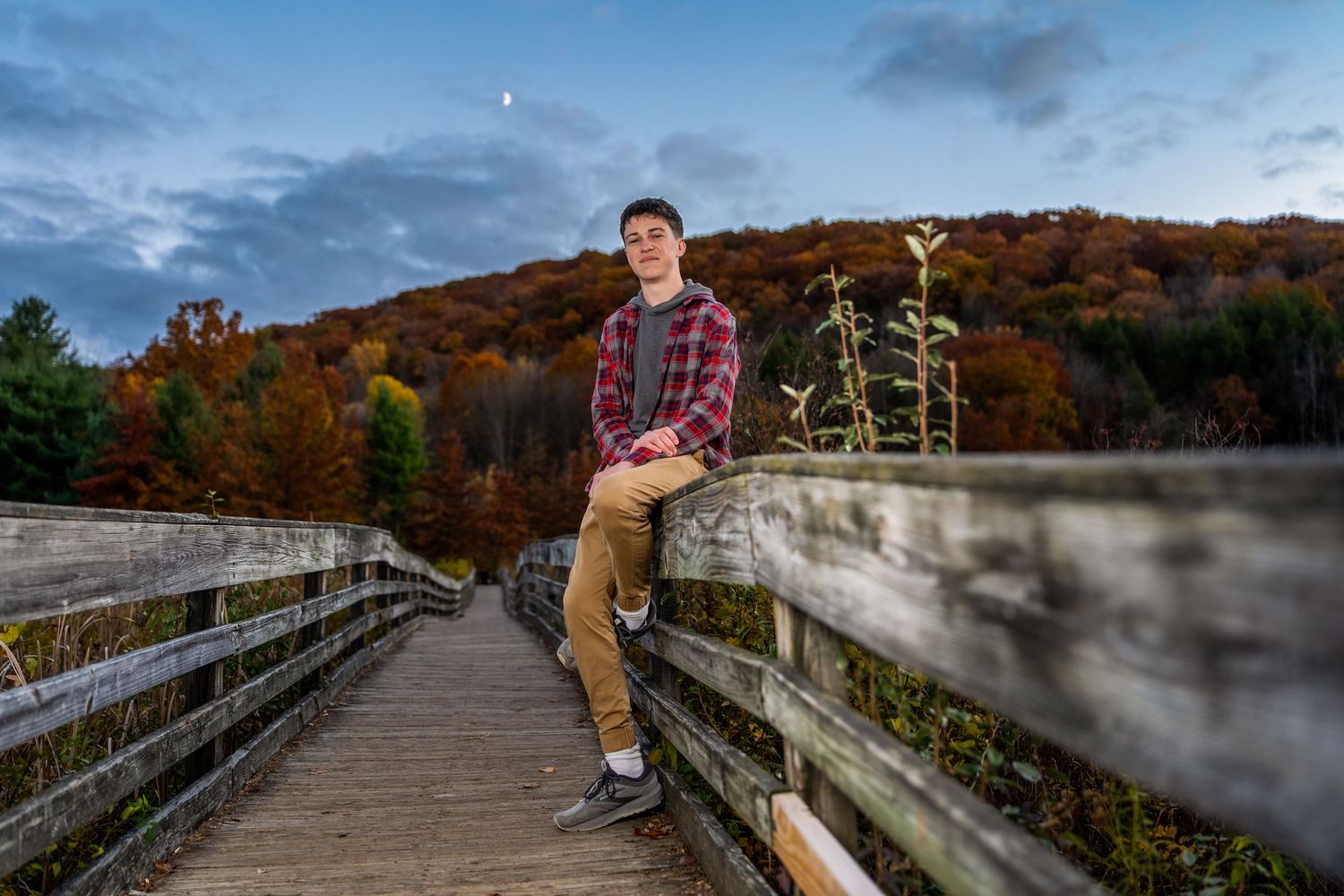 senior photo on a wooden bridge with trees and nature in the background, moon visible in the sky