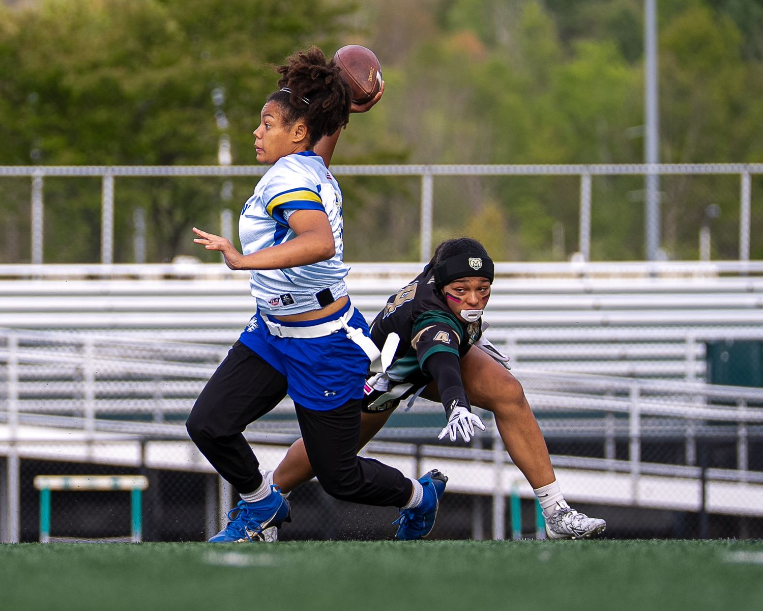 Two female flag football players compete on a field, one catching a pass while the other defends during a game.