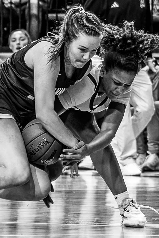 Two female basketball players battle for possession of a Spalding ball in an intense black and white action photo.