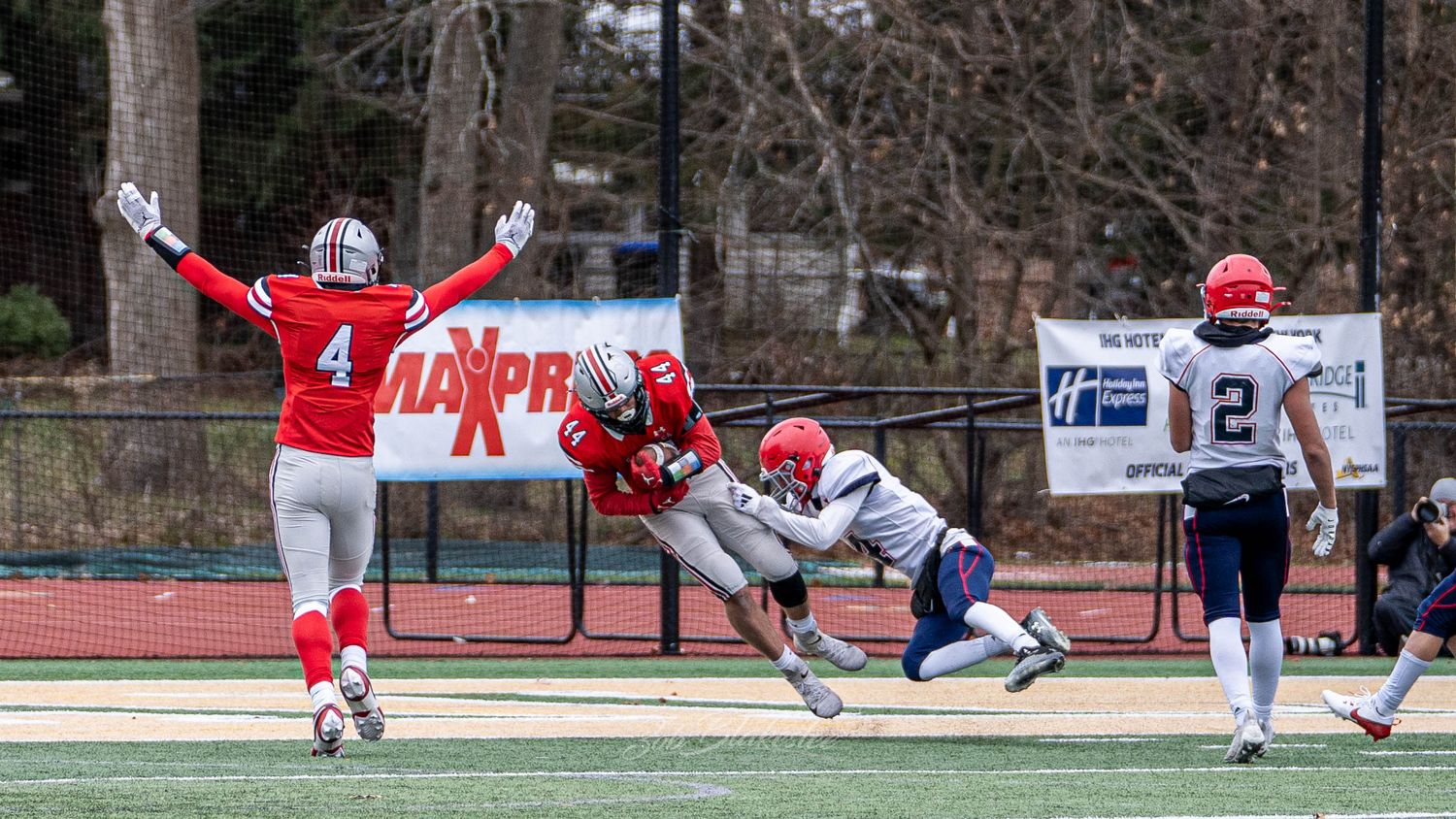 Football player dives to make a catch while defenders react during a competitive high school game.