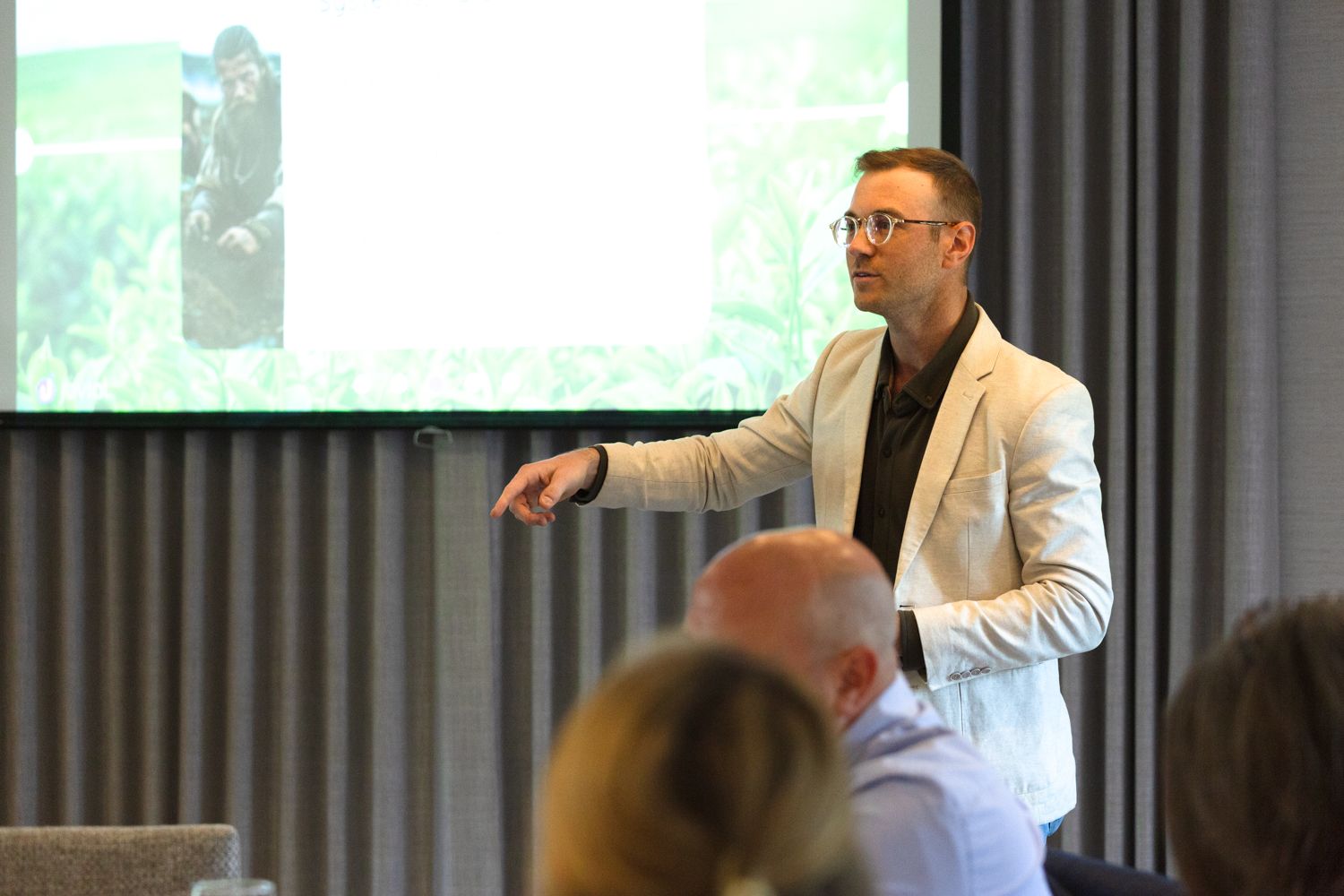Man in white blazer presents to an audience in front of a projected nature image at a conference.
