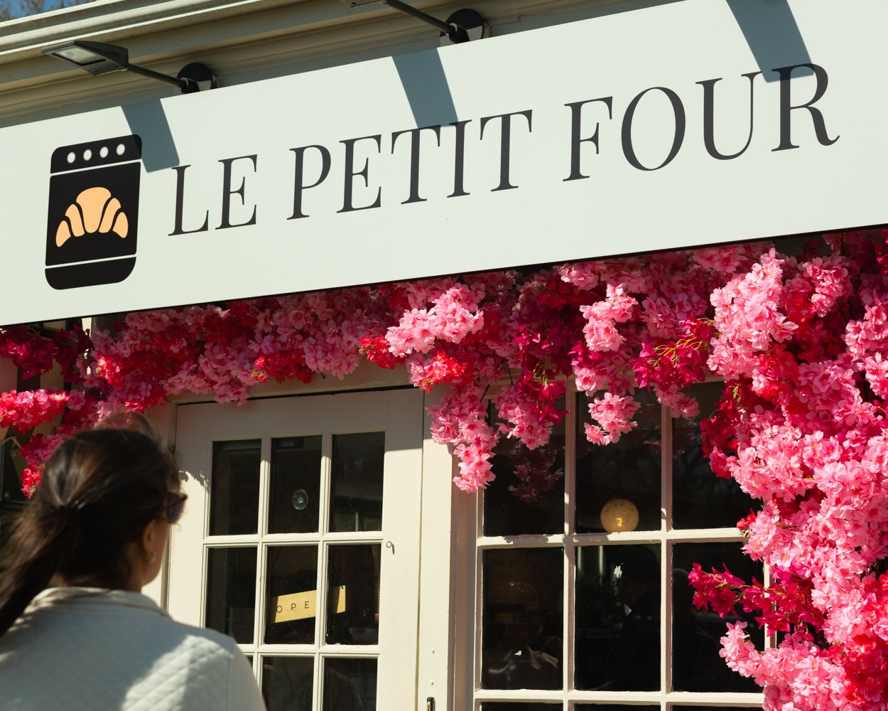 Pink floral facade of Le Petit Four bakery with a croissant logo on a white sign.