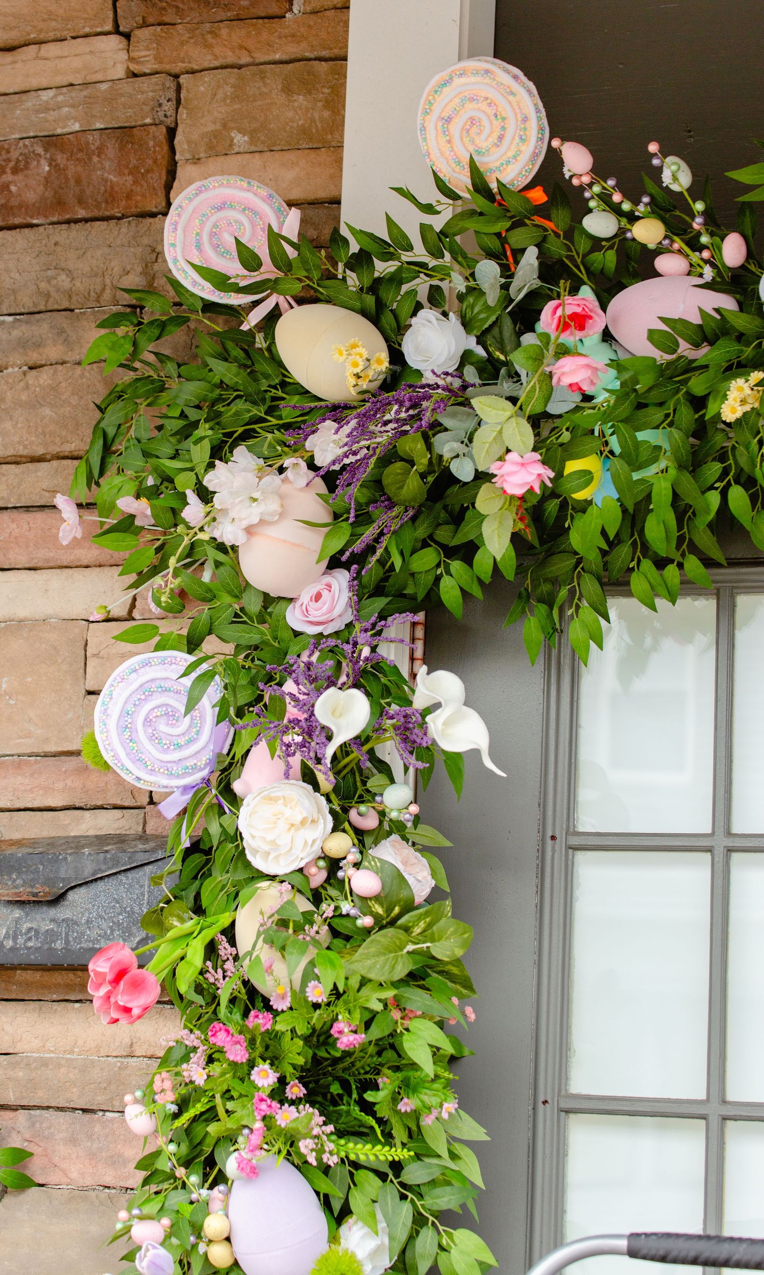 Easter garland with pastel eggs, lollipops, and flowers decorating a stone building entrance.