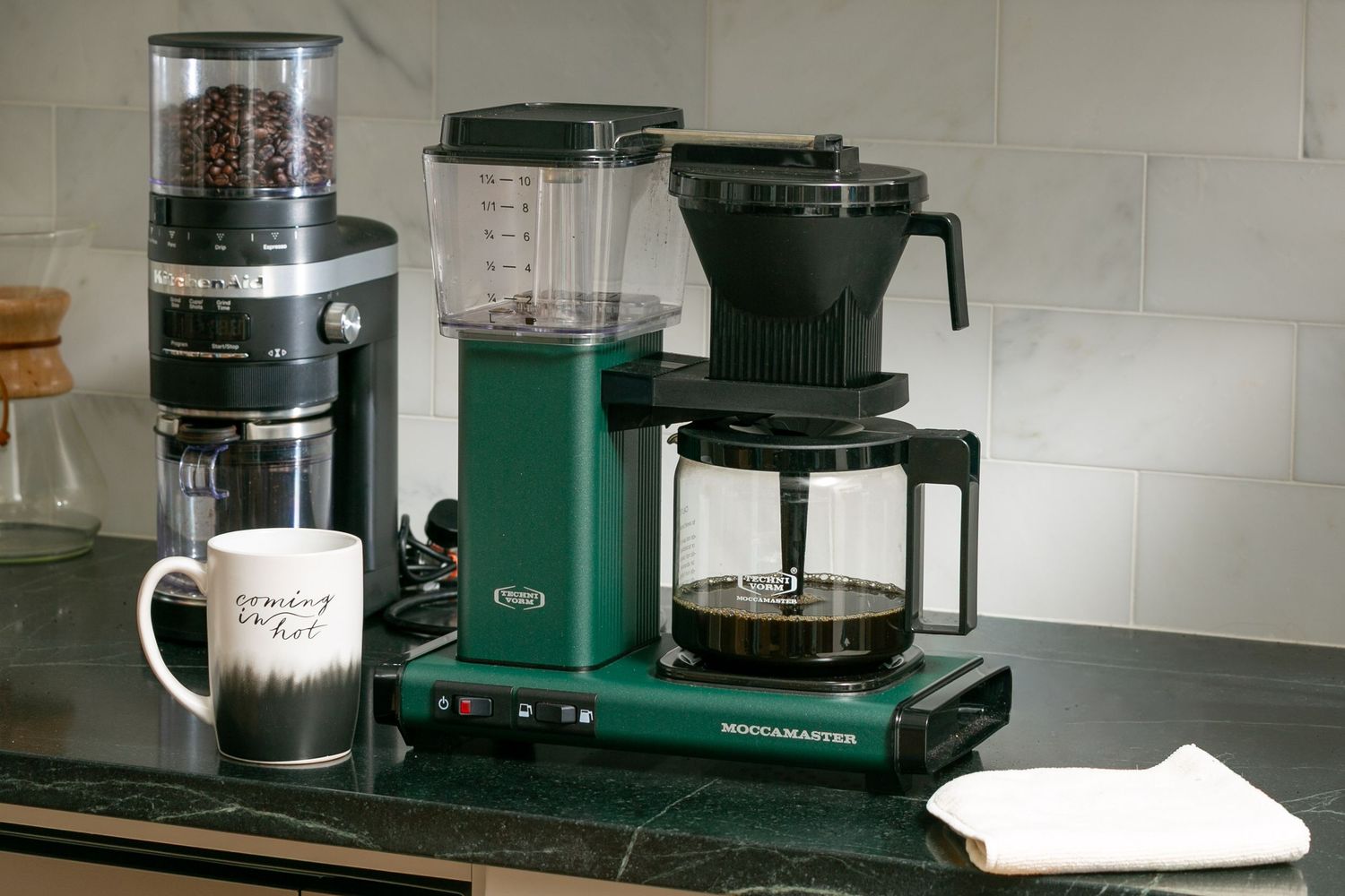 Green Moccamaster drip coffee maker with grinder and glass carafe on a kitchen counter.