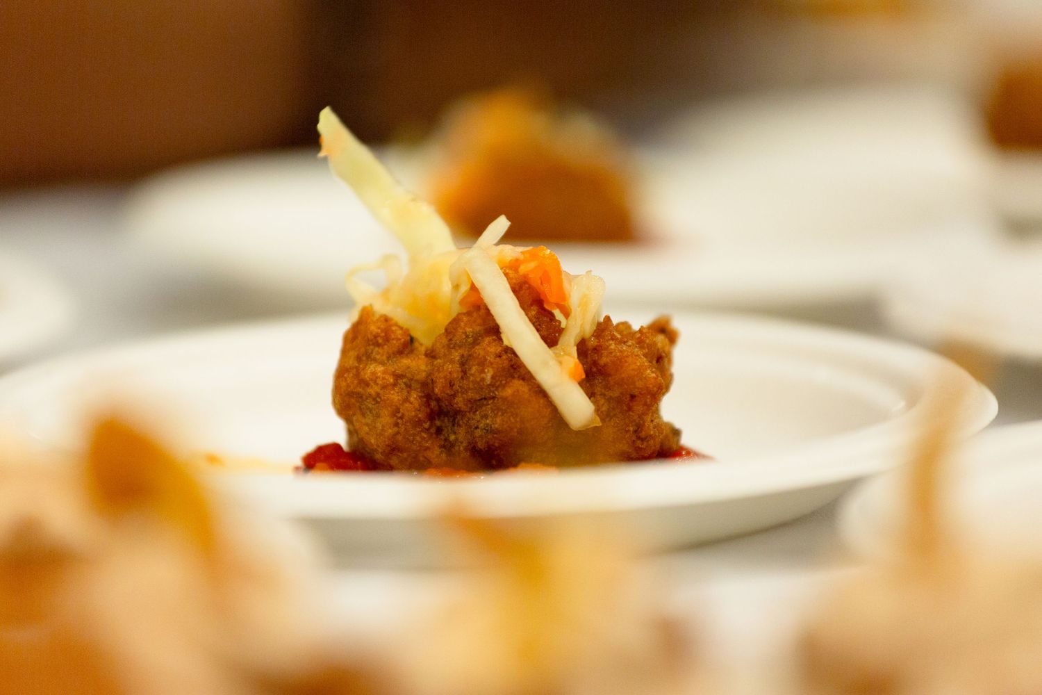 Close-up of a crispy fried appetizer topped with shaved cheese on a small white plate.