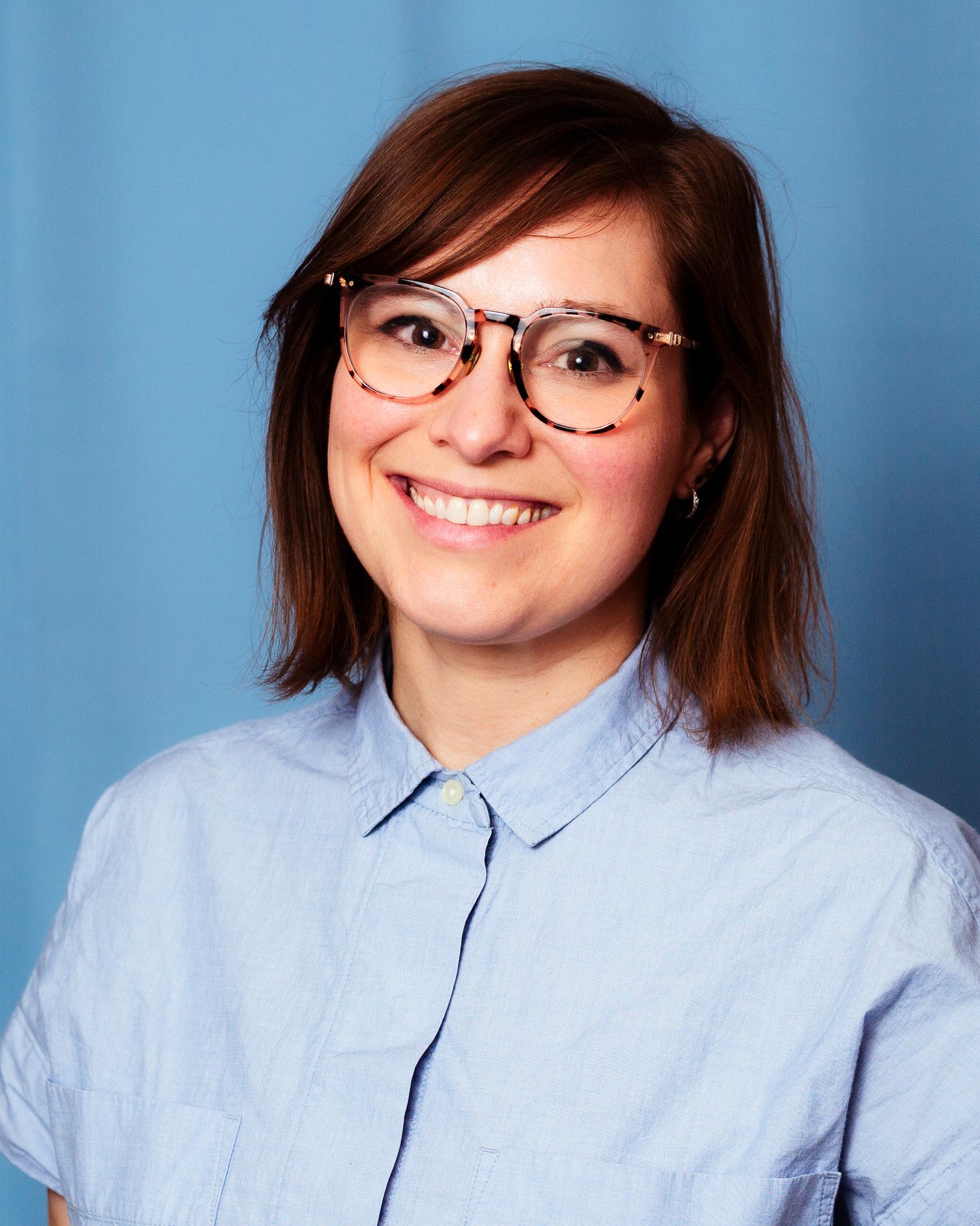 Young woman with glasses and bob haircut smiling against blue background.