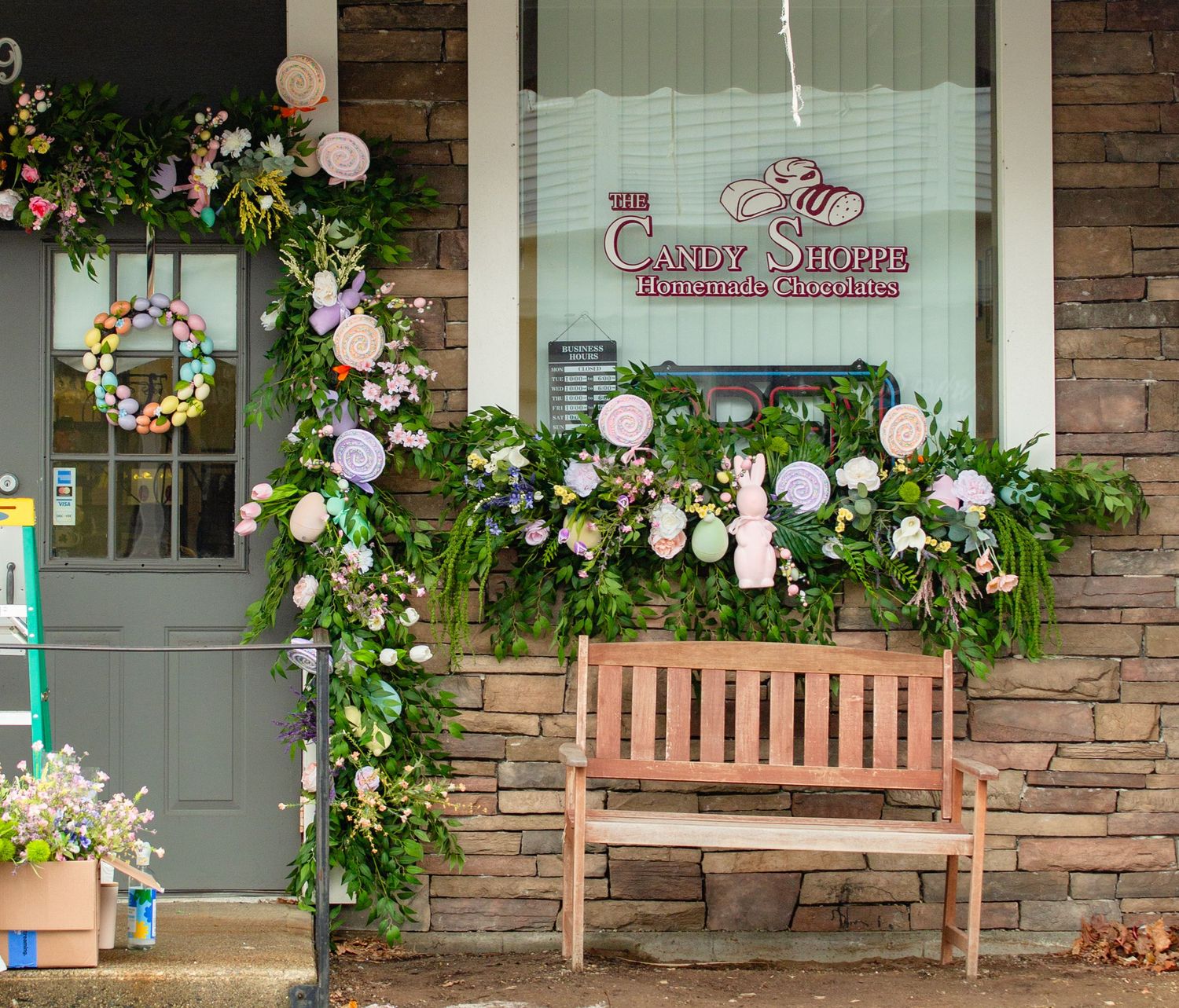 The Candy Shoppe storefront decorated with Easter spring floral garlands, wreaths, and a wooden bench outside.