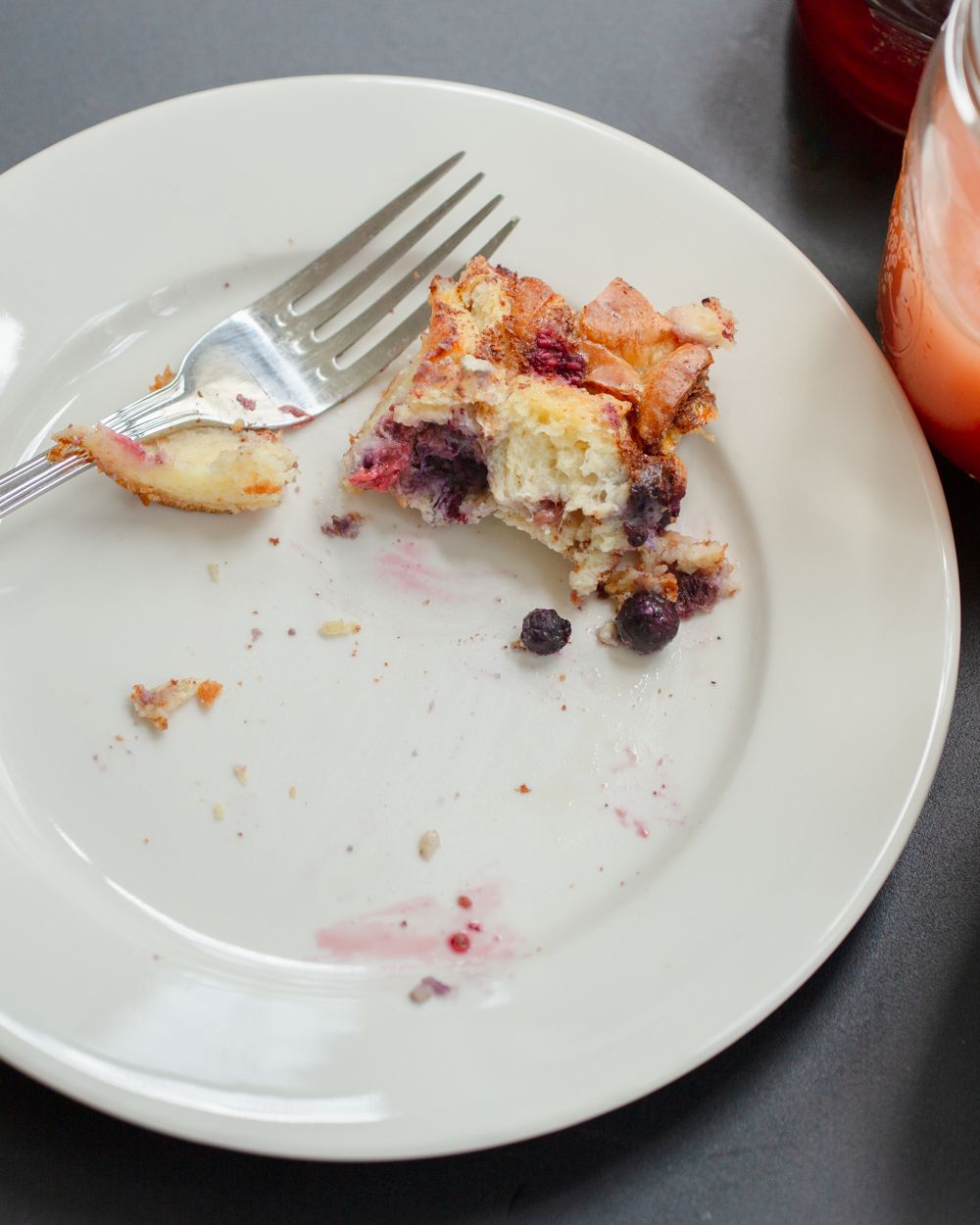 Partially eaten blueberry French toast casserole on a white plate with a fork on a gray surface.