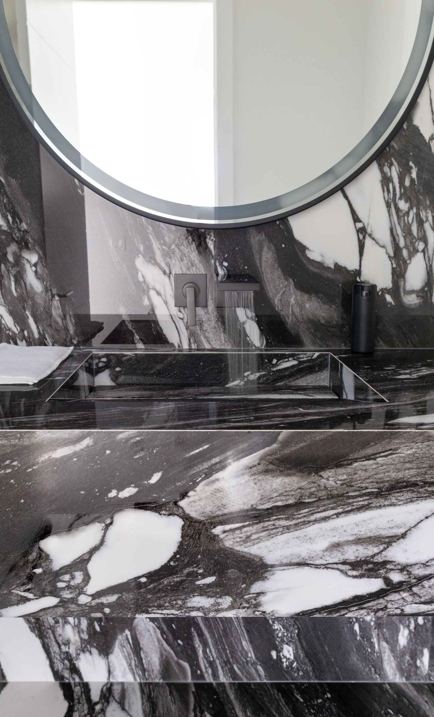 Luxurious black and white marble bathroom vanity with round mirror and dramatic veining detail.
