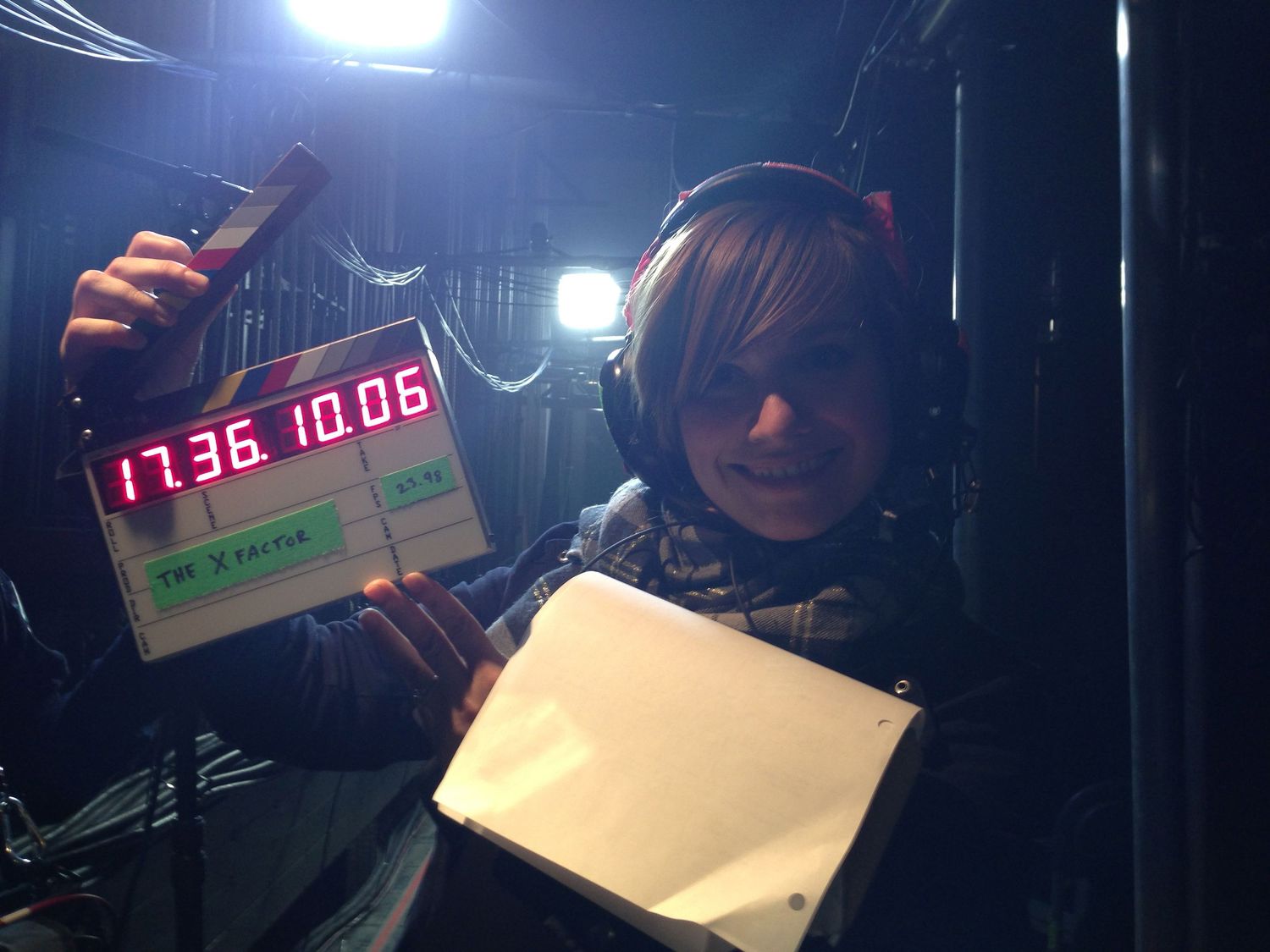 Person holding a film clapperboard with timecode display in a dark production set environment.