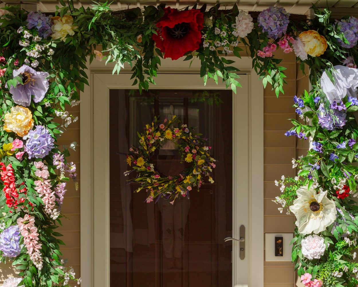 Front door decorated with a lush floral arch garland and spring wreath in full bloom.