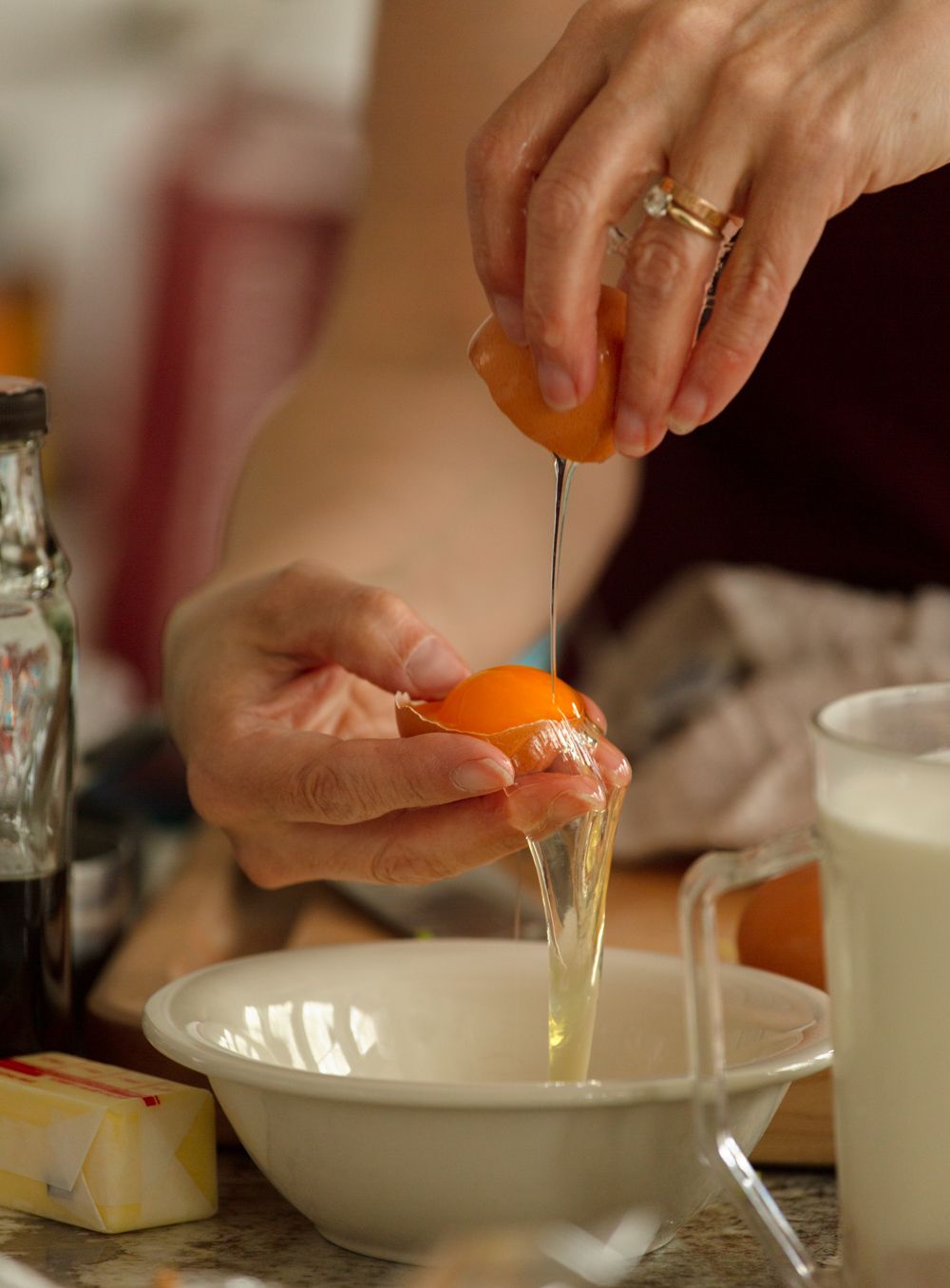 Close-up of hands cracking a fresh egg into a white bowl with milk and butter nearby.