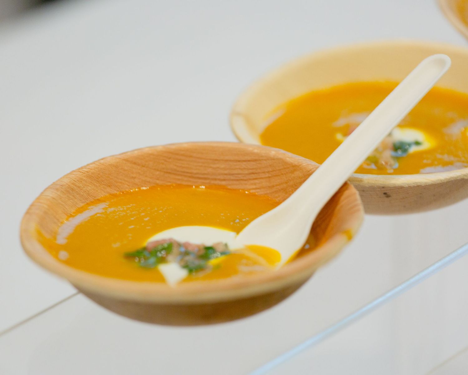 Two wooden bowls of creamy butternut squash soup garnished with herbs and cream.